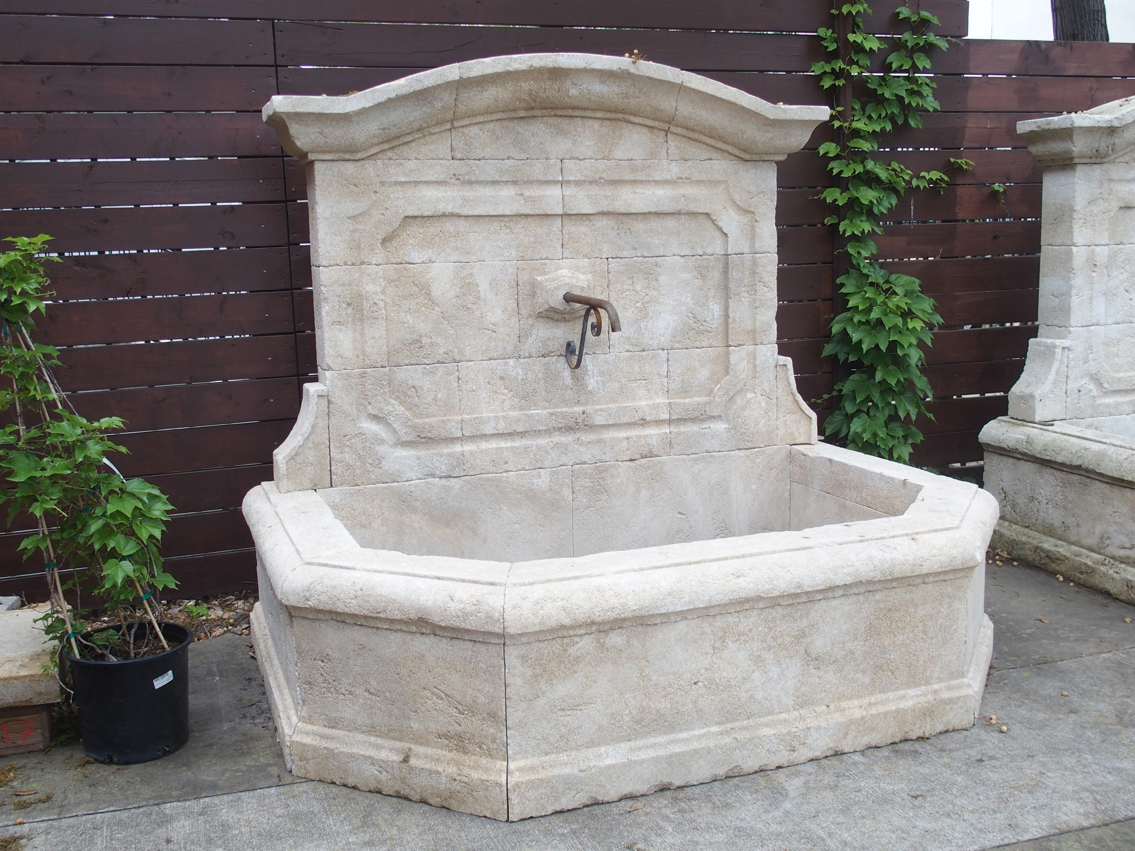Comprised of 25 pieces of stone, this limestone wall fountain was hand-carved in Provence, France, in the 2000’s. The large half-octagonal basin (comprised of 12 stones, including five capstones) features thick quarter round top edges coupled with a