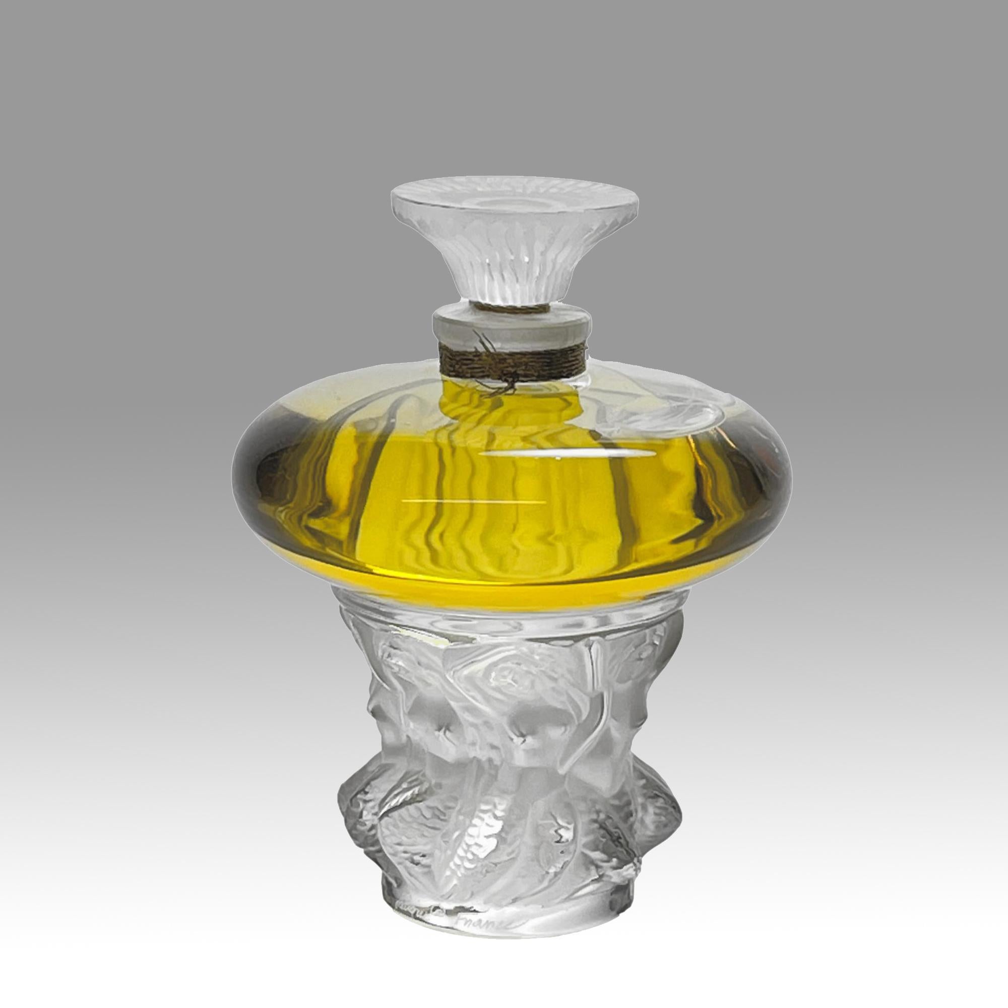 An attractive limited edition clear and frosted glass scent bottle, the clear glass body containing the original Lalique perfume supported by a frosted glass column decorated with dancing sirens around the circumference with fine detail, signed