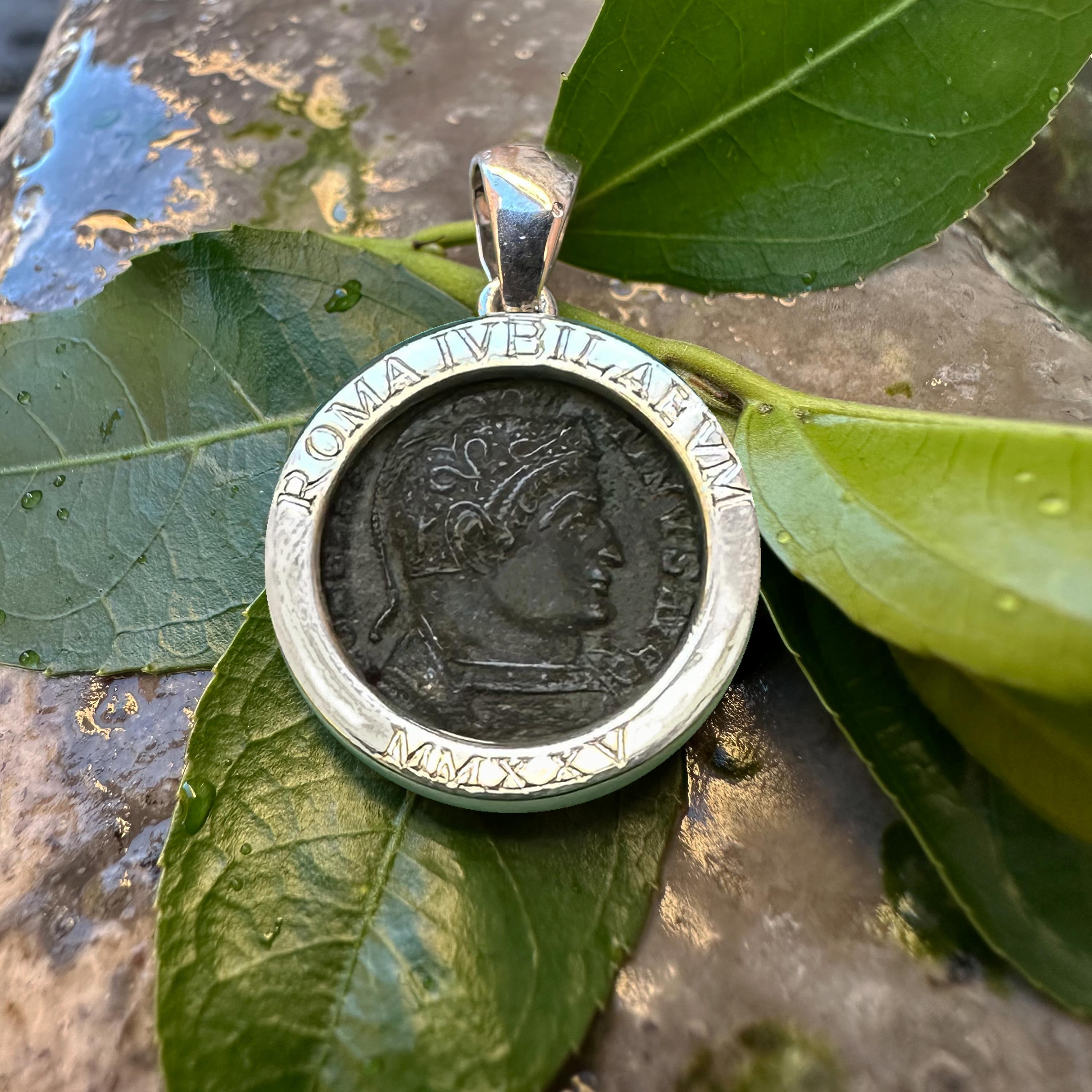 Dieser Anhänger aus Sterlingsilber enthält eine echte römische Bronzemünze aus dem 4. Jahrhundert n. Chr. mit dem Konterfei von Kaiser Konstantin dem Großen. Auf der Rückseite der Münze ist eine Himmelskugel abgebildet, die auf einem Altar mit der