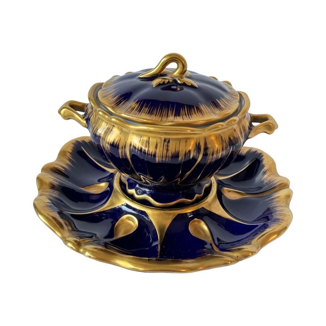 An exceptional Limoges porcelain sauce dish with lid and matching tray, featuring a rich cobalt blue glaze and luxurious hand-painted gold detailing. The bold gold brushwork contrasts beautifully against the deep blue surface, creating an elegant