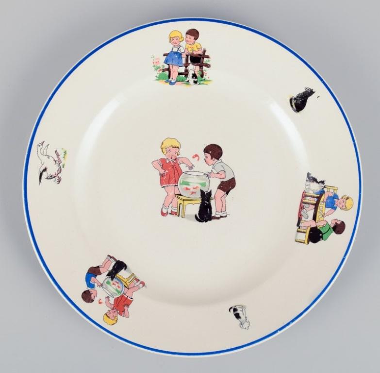 Limoges, Digoin & Sarreguemines, France. Children's porcelain dinnerware consisting of a plate, two small dishes, and a cup. 
Motifs of children at play.
From the 1930s/1940s.
In very good condition with signs of use.
The plate and the large dish