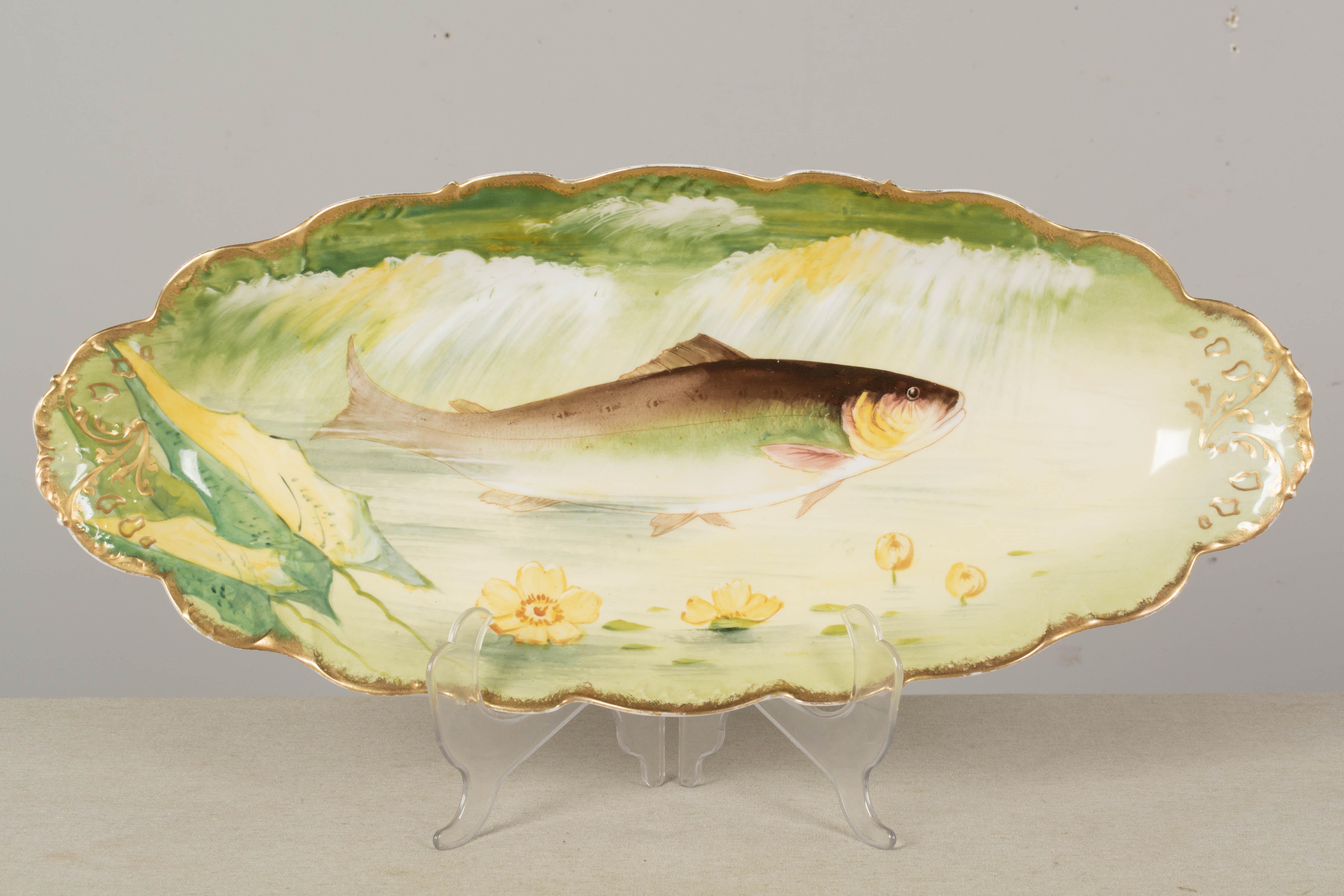An early 20th century French Limoges porcelain fish platter and 12 plates, each hand-painted in green and yellow with gilt edge. Mark to underside: Elite Works Limoges France. (Red print indicating 1900-1914 run) Excellent condition with only one