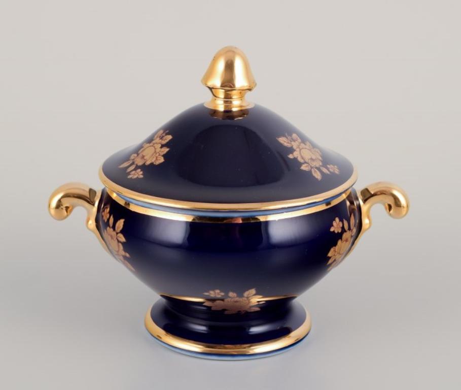 Limoges, France. Coffee cup, sugar bowl, and creamer in porcelain decorated with 22-karat gold leaf and beautiful royal blue glaze. Scène galante. 
Approximately 1970.
Provenance: From a large French private collection of Limoges