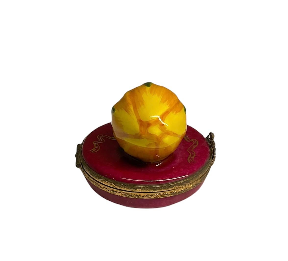 This is a Limoges France Faberge Porcelain rose bud trinket hinged box. It is depicting a large yellow rose bud at the top of an oval cranberry color box. This top also has a gold hand painted laurel wreath with a bow and long ribbons. Inside the