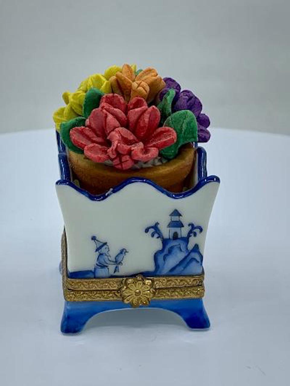 Collectible and very unique, Limoges porcelain miniature trinket box is handmade and hand painted in France and features beautiful multi colored three dimensional realistic flowers in a pot which sits on the top of the blue and white willow design
