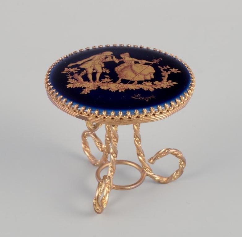 Limoges, Frankreich. Miniaturtisch und Stühle aus Messing und Porzellan, verziert mit 22-karätigem Blattgold und einer schönen königsblauen Glasur. Galanter Schauplatz. 
Ungefähr 1970.
Provenienz: Aus einer großen französischen Privatsammlung von