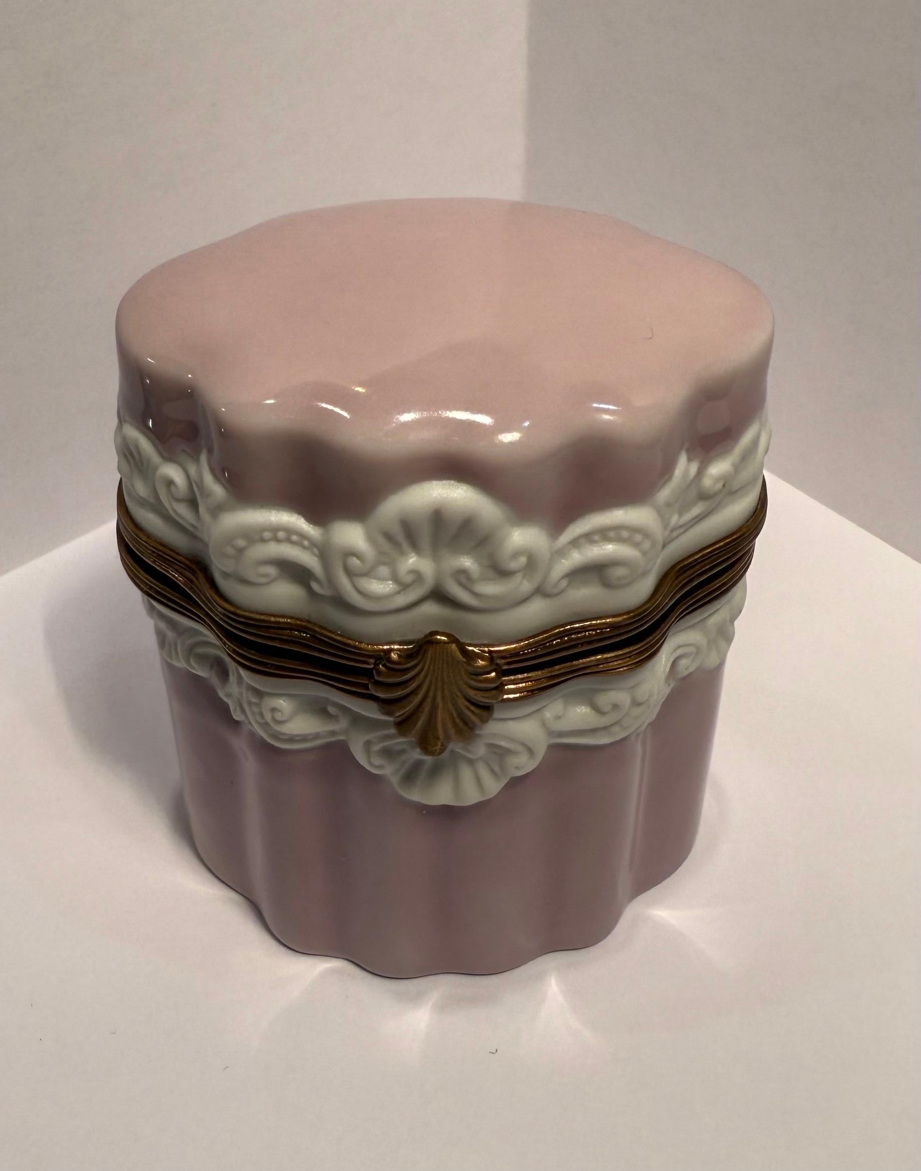 Preciosa caja de baratijas ovalada de porcelana de Limoges con forma festoneada, hecha y pintada a mano en un suave color malva y con adornos de porcelana en alto relieve de rocaille blanca y motivos de conchas. La caja presenta herrajes de metal