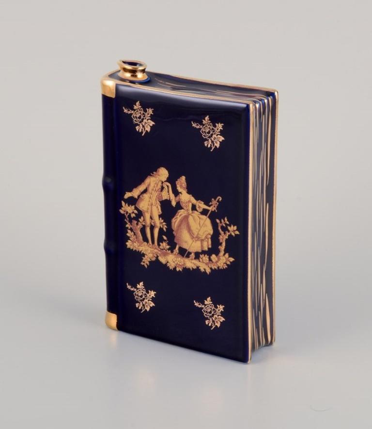 Limoges, Francia. Petaca de porcelana con forma de libro, decorada con pan de oro de 22 quilates y esmalte azul real. Escena galante.
Aproximadamente desde 1970.
Procedencia: Procedente de una gran colección privada francesa de porcelana de