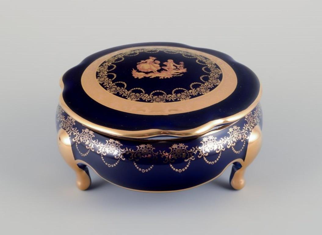 Limoges, France. Two lidded porcelain boxes / jars decorated with 22-karat gold leaf and featuring a beautiful royal blue glaze with a Scène galante.
Approximately 1970.
Provenance: From a large French private collection of Limoges