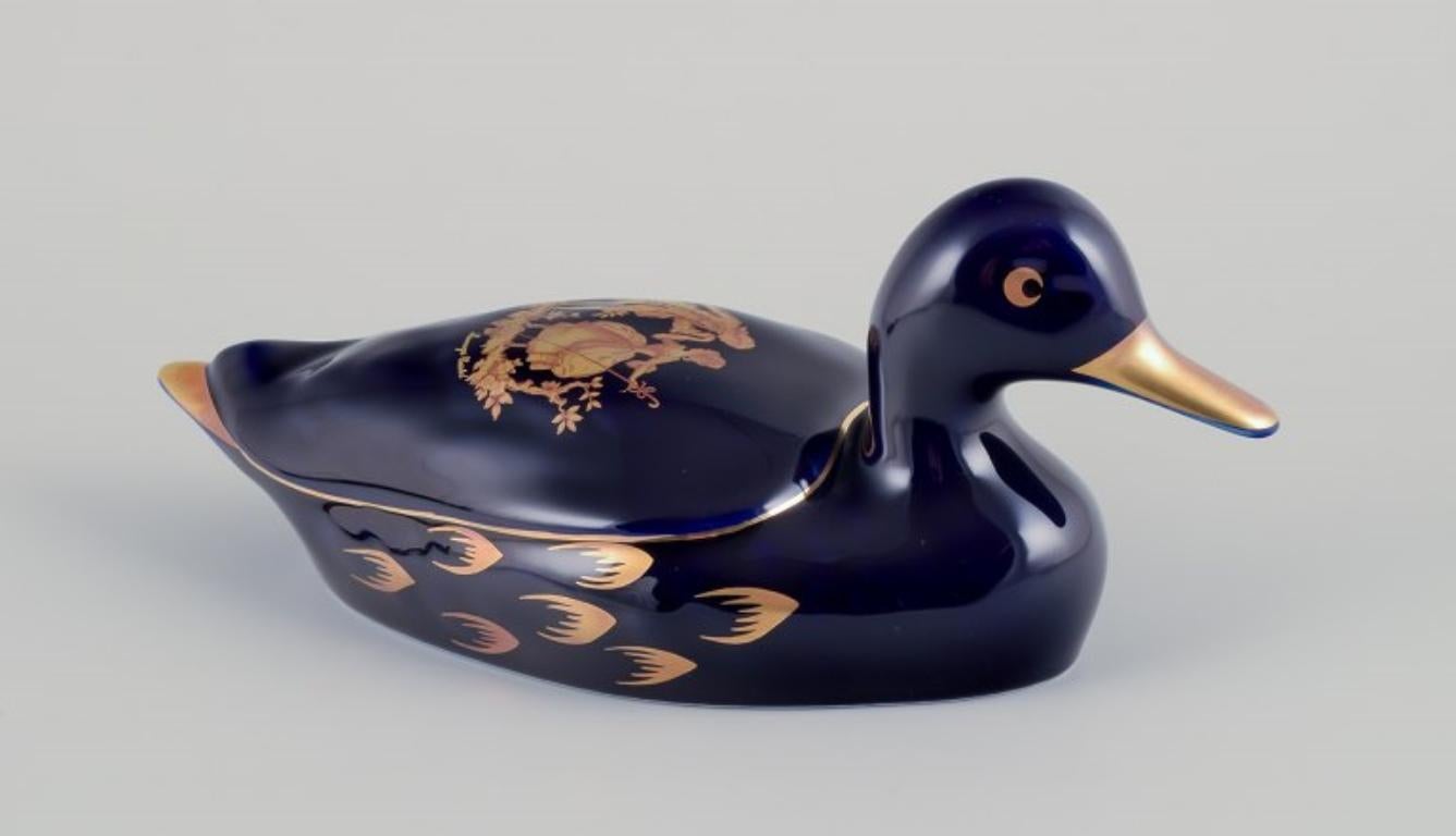 Limoges, Frankreich. Zwei Enten aus Porzellan, verziert mit 22-karätigem Blattgold und einer schönen königsblauen Glasur. Galanter Schauplatz. 
Ungefähr 1970.
Provenienz: Aus einer großen französischen Privatsammlung von