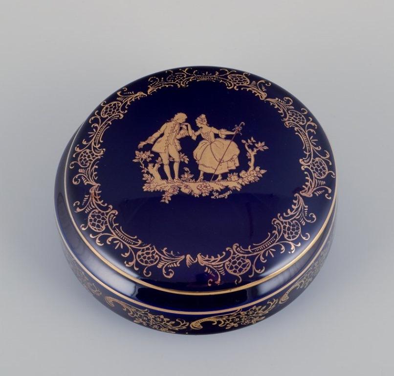 Limoges, Francia. Dos tarros/cajas redondos con tapa, de porcelana decorada con pan de oro de 22 quilates y hermoso vidriado azul real. Escena galante. 
Aproximadamente 1970.
Procedencia: Procedente de una gran colección privada francesa de