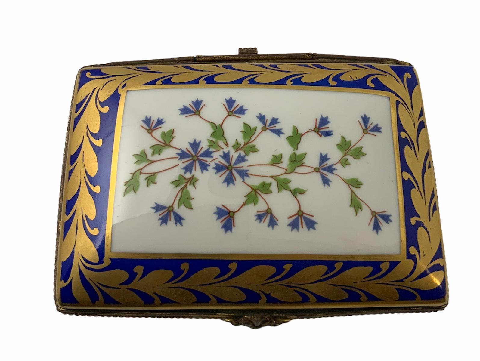 This is a rectangular hand painted porcelain box embellished by gilded olives leaves garland & blue flowers foliage. The rim of the lid & box is decorated by some golden beading chain. Inside, the lid is also hand painted by a branch of flowers.