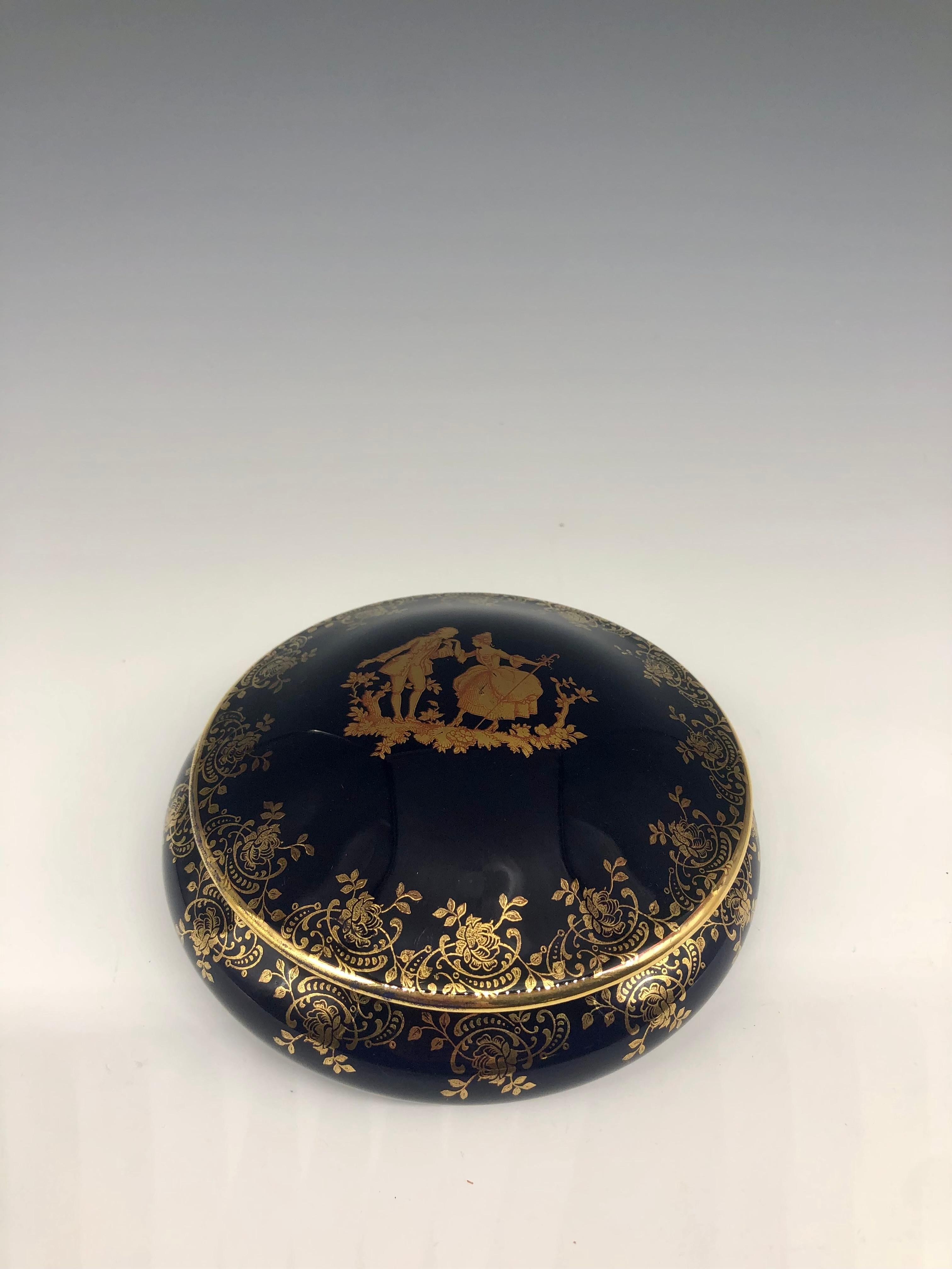 Beautiful vintage cobalt blue lidded porcelain trinket jewelry box with gold hand-painted floral decorative rim. The central illustration is of a couple dressed in Louis XVI period style dress, with the male kissing the hand of a woman curtsying and