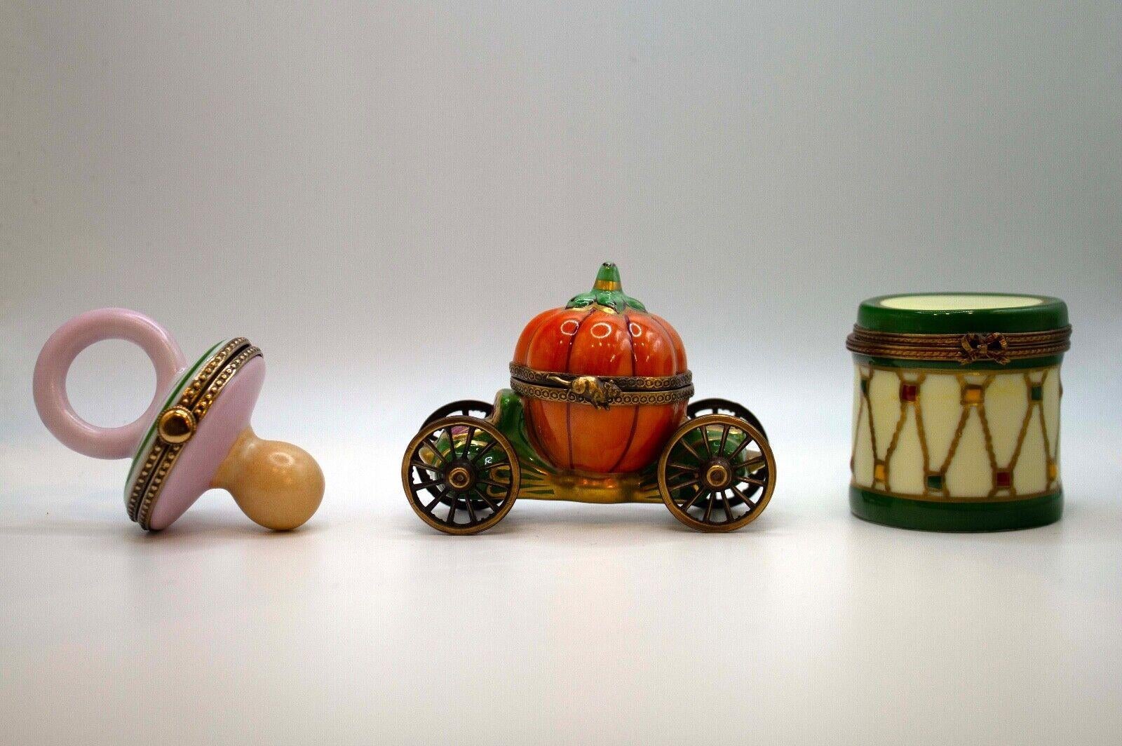 An adorable set of miniature porcelain collectable boxes by Limoges - featuring a pacifier with rabbit design, Cinderella's pumpkin carriage, and a green drum. Each one is artfully hand-painted with exquisite detailing and brilliant colors. The box
