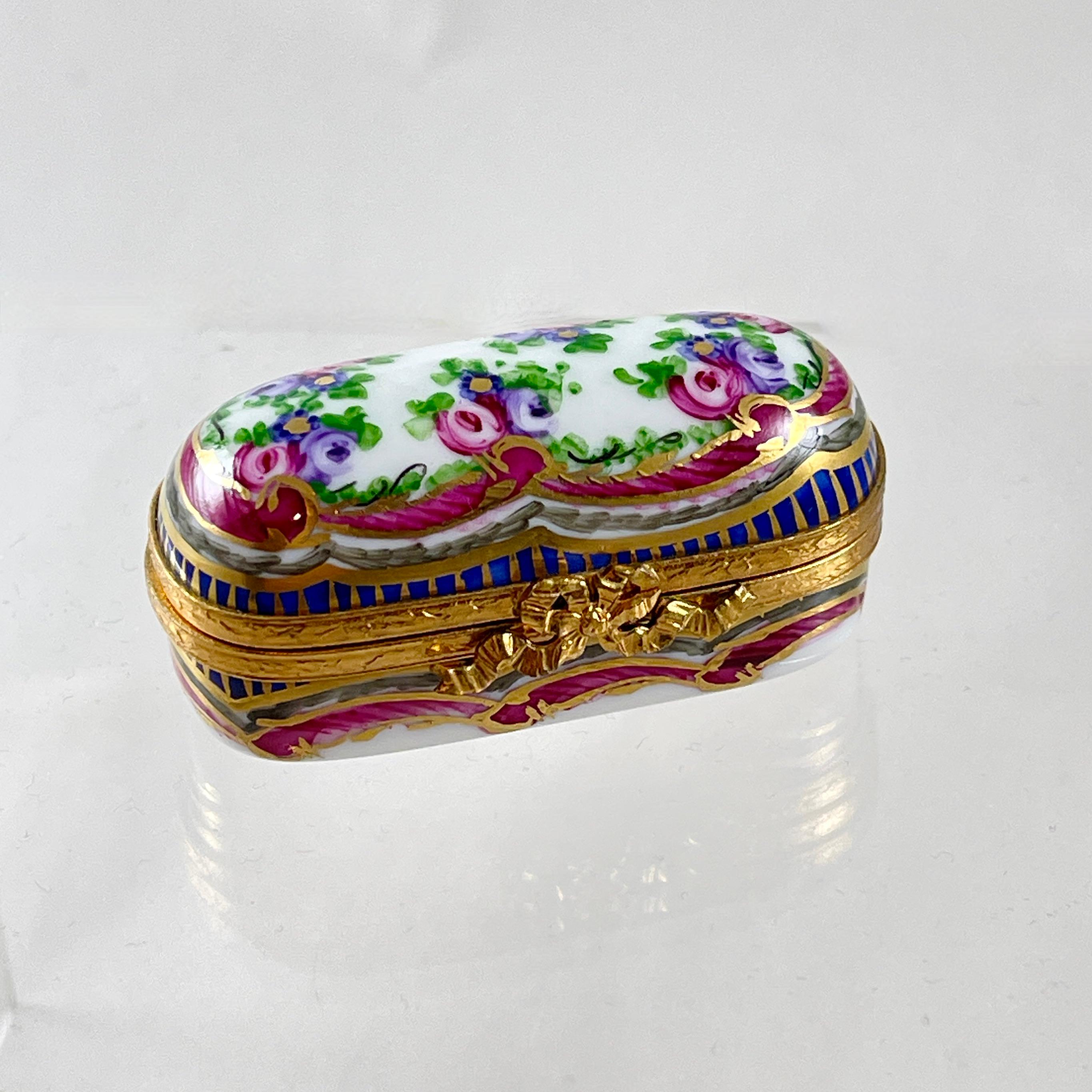 De Limoges (Francia), caja de baratijas esmaltada a mano, del tamaño adecuado para contener agujas de coser o alfileres, hacia 1970-1980.

La caja de metal cobrizo con tirantes tiene un diseño pintado a mano de rosas y volutas acentuado en azul