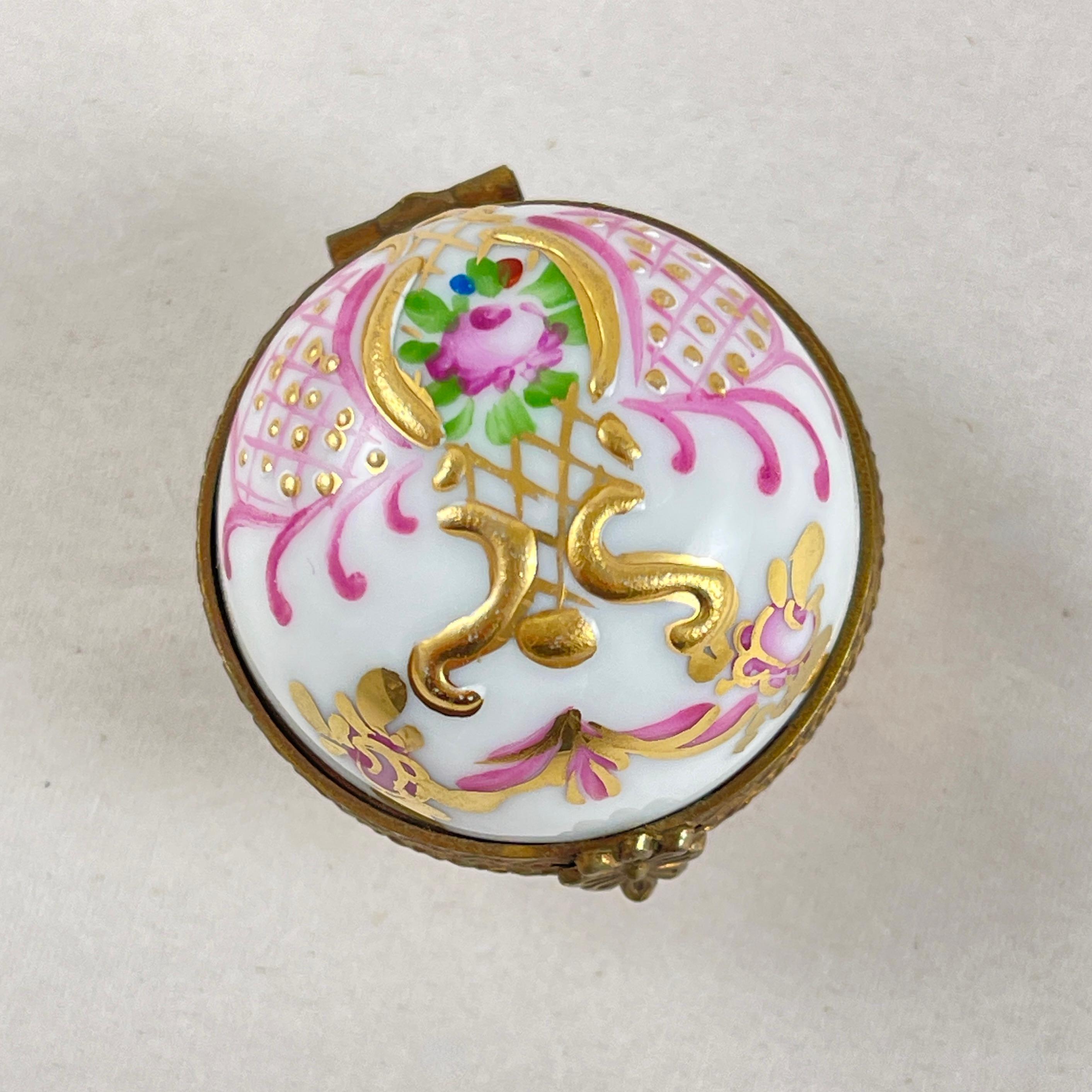 A hand painted Limoges porcelain trinket box, France, circa 1970-1980.

The round box is braced with a metal frame featuring a floral clasp.
Decorated with a pink rose and gilded scrolling.

The interior shows gilded feathers on both the lid and the