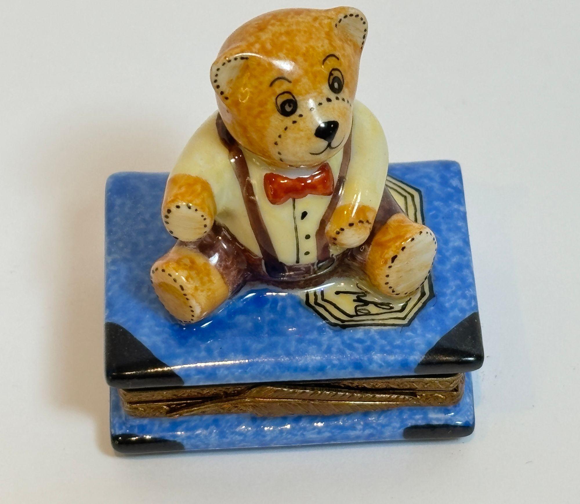 Vintage Limoges Porcelain Box with Teddy Bear on Book, Hand-Painted, France, ca. 20th Century
A charming hand-painted Limoges porcelain trinket box featuring an adorable teddy bear seated atop a detailed blue book, inscribed “Cahier d’orthographe.”