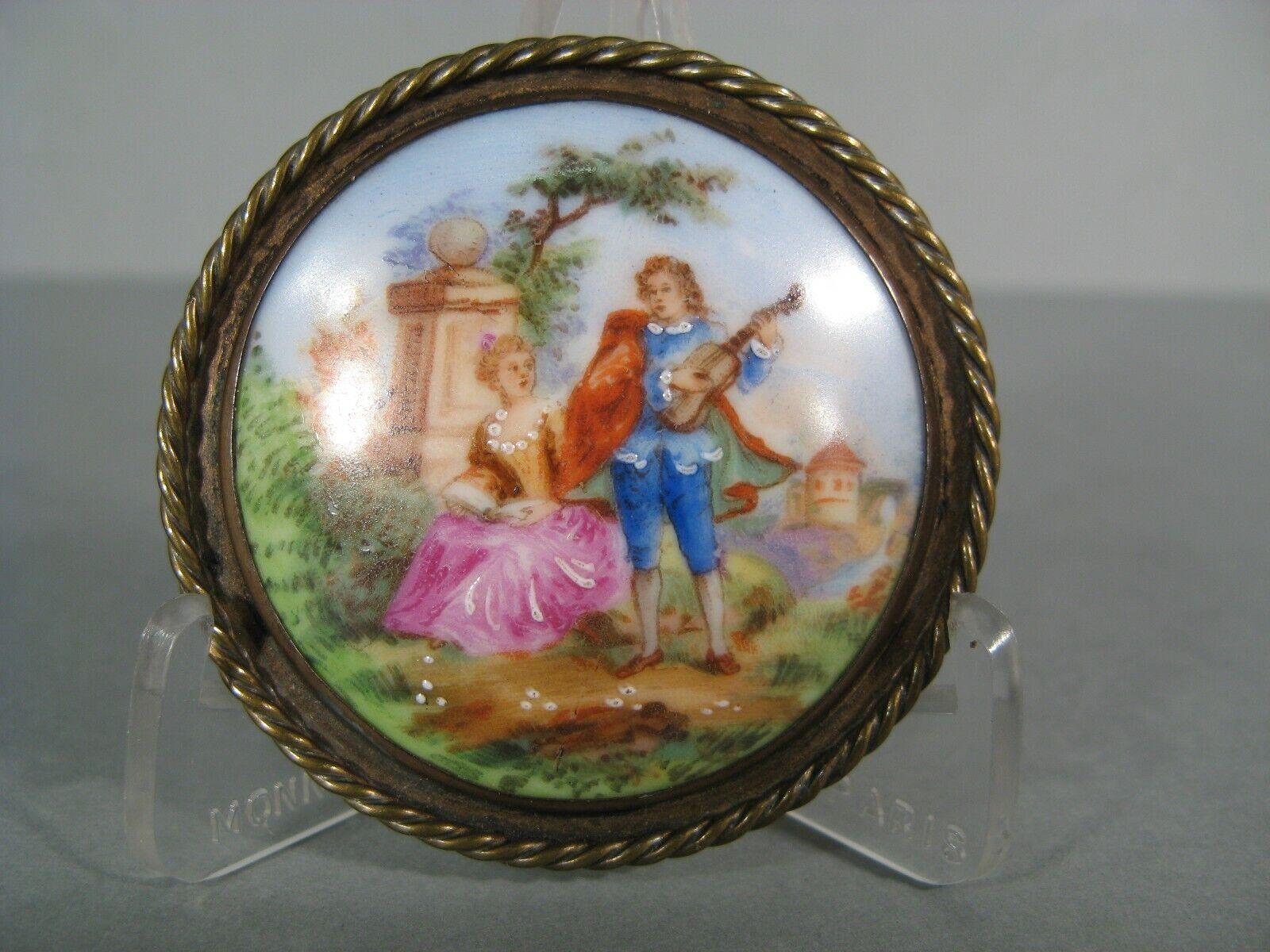 Este encantador broche antiguo presenta una pintura en miniatura esmaltada sobre porcelana de Limoges, que representa una escena romántica con un juglar y una joven de calidad. La porcelana está engastada en un broche de latón, marcado 