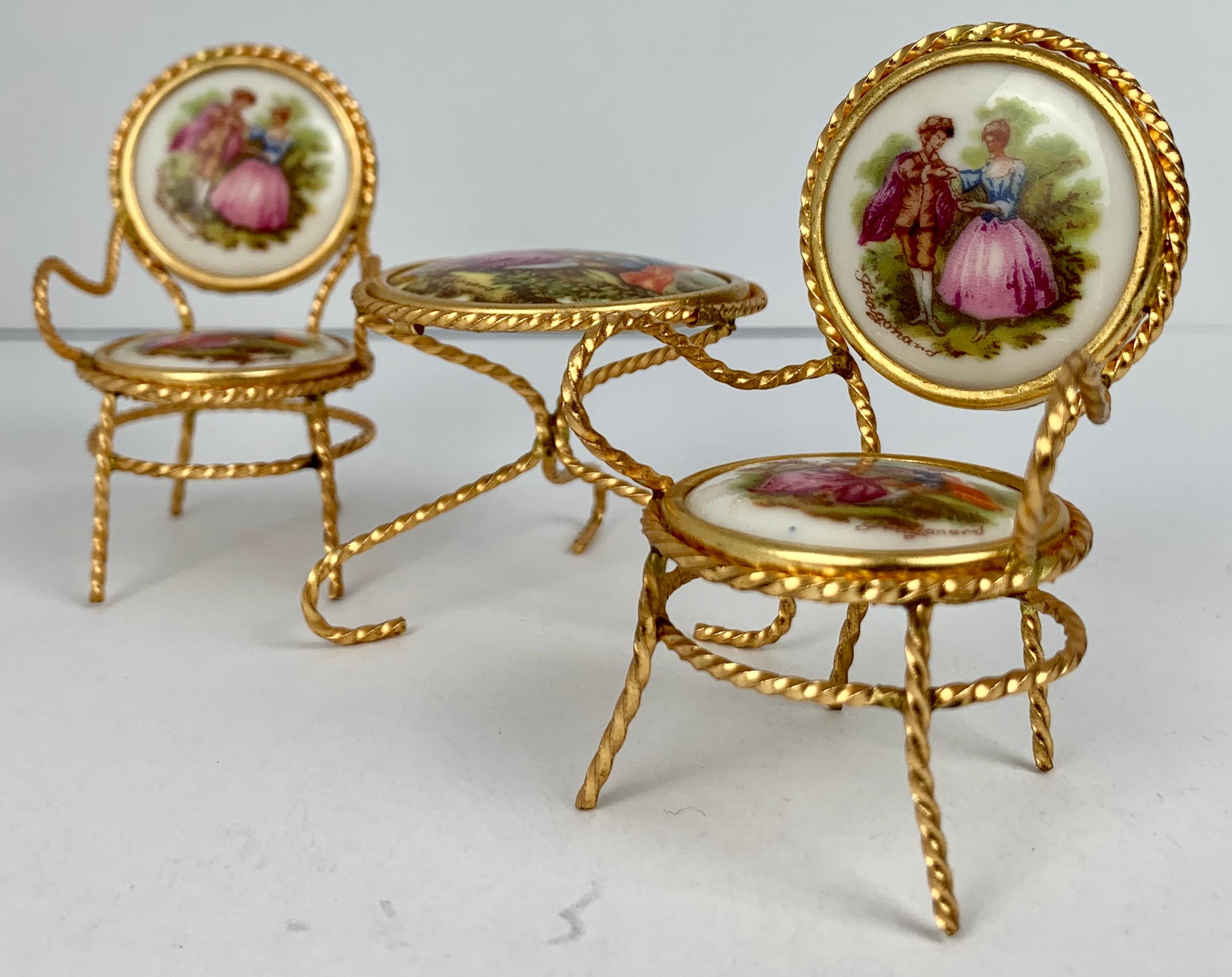 Suite of miniature Limoges porcelain furniture. The pair of armchairs and table are set with signed Limoges porcelain plaques after Honore Fragonard. The frames are gilt metal. The set is in perfect condition as they sat in a vitrine since they were