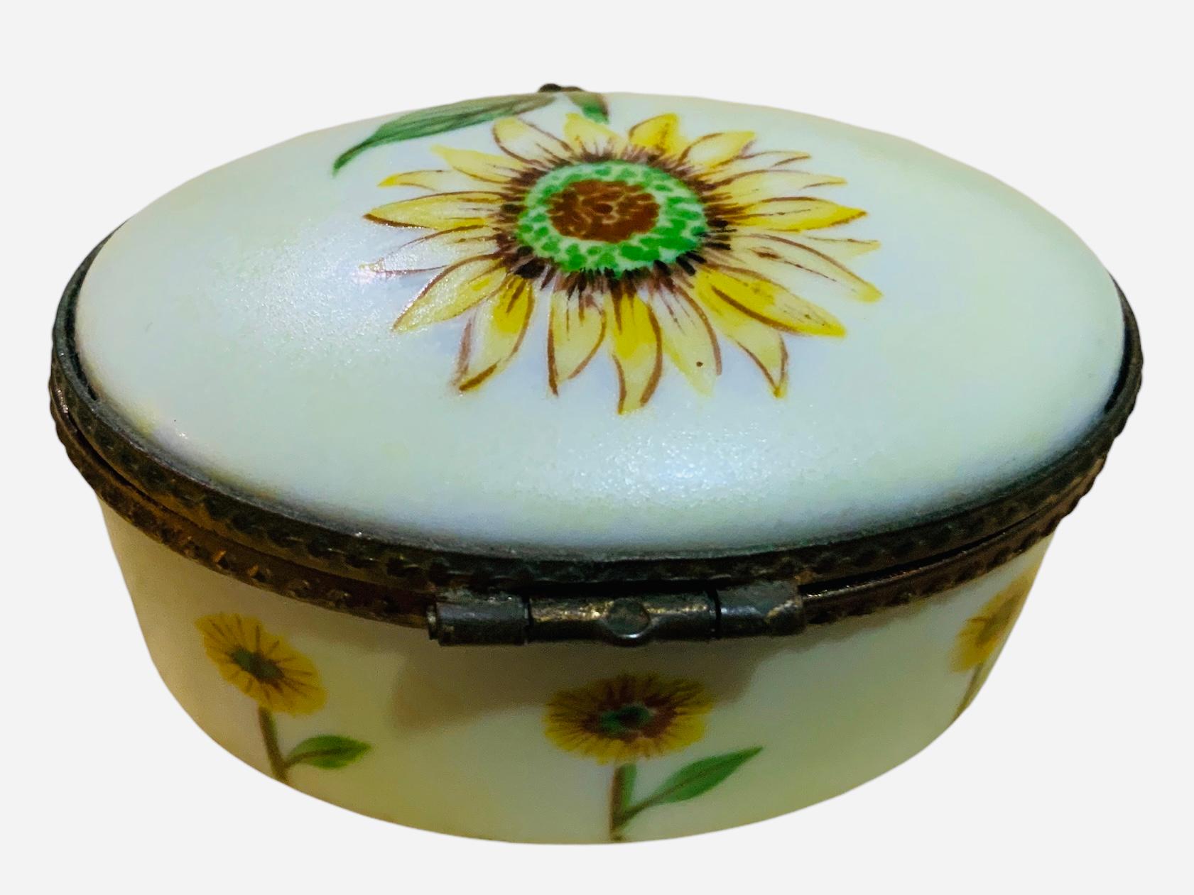Se trata de una caja de baratijas ovalada de porcelana de Limoges. Su fondo está pintado a mano de amarillo claro. La parte superior de la tapa abatible está adornada con un gran girasol y los laterales de su base con varios pequeños. Dentro de la