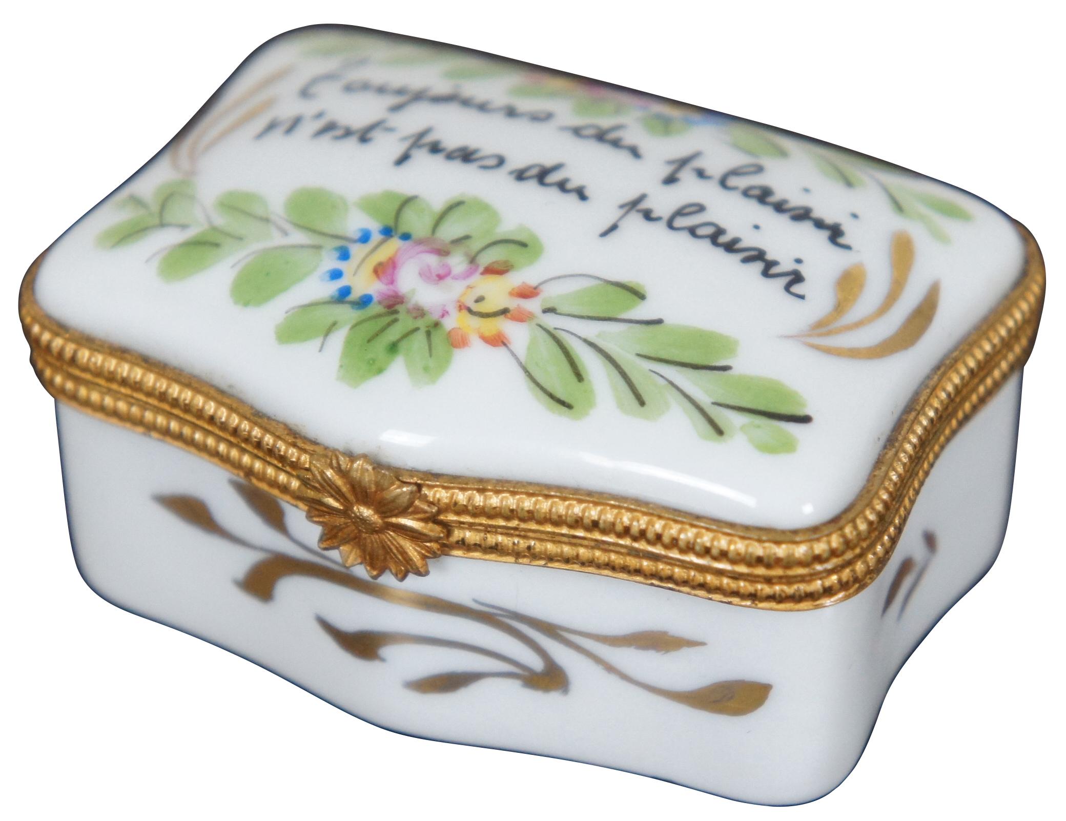Vintage Limoges porcelain trinket or pill box hand painted with an array of flowers and the phrase “Toujour du Plaisir N’est-pas du Plaisir” (French for “Pleasure Always Isn’t Pleasure”).
  