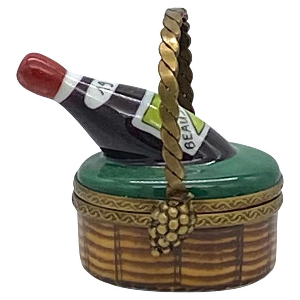This is a hand painted Limoges trinket box with a wine bottle nestled in a basket. The bottle of Beaujolais 1975 is in a picnic basket with a detailed handle. On the bottom is 