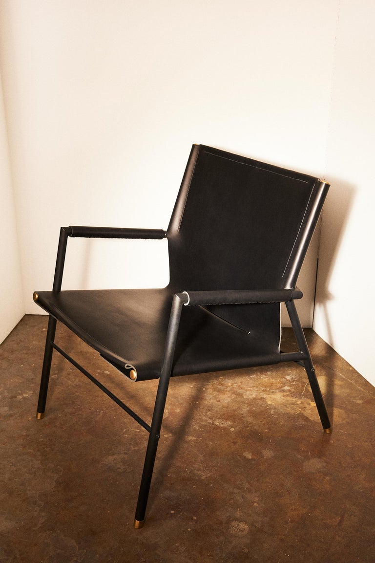 A single grain leather hide, tensioned with cord lacing underneath the seat, makes up the expanse of this richly textured chair. The blackened frame is patinated and lacquered by hand. The rounded bronze feet and caps complete the