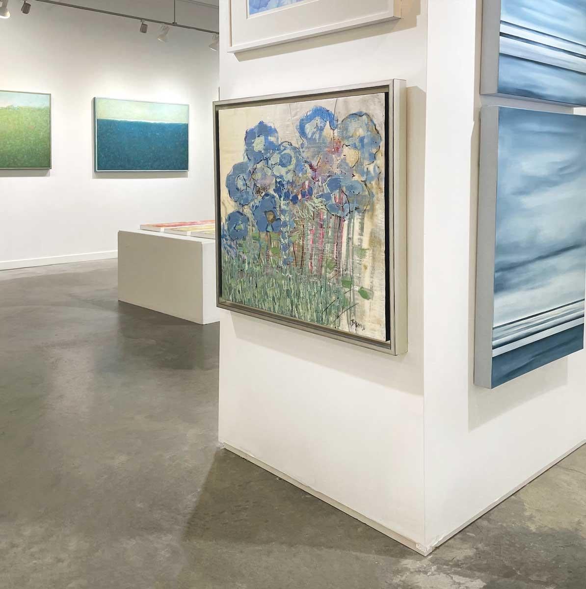 This abstract encaustic painting by artist Linda Bigness features a highly textured floral composition. Blue floral shapes are clustered at the center of the piece, with green layers and strokes beneath it and purple and pink accents visible around