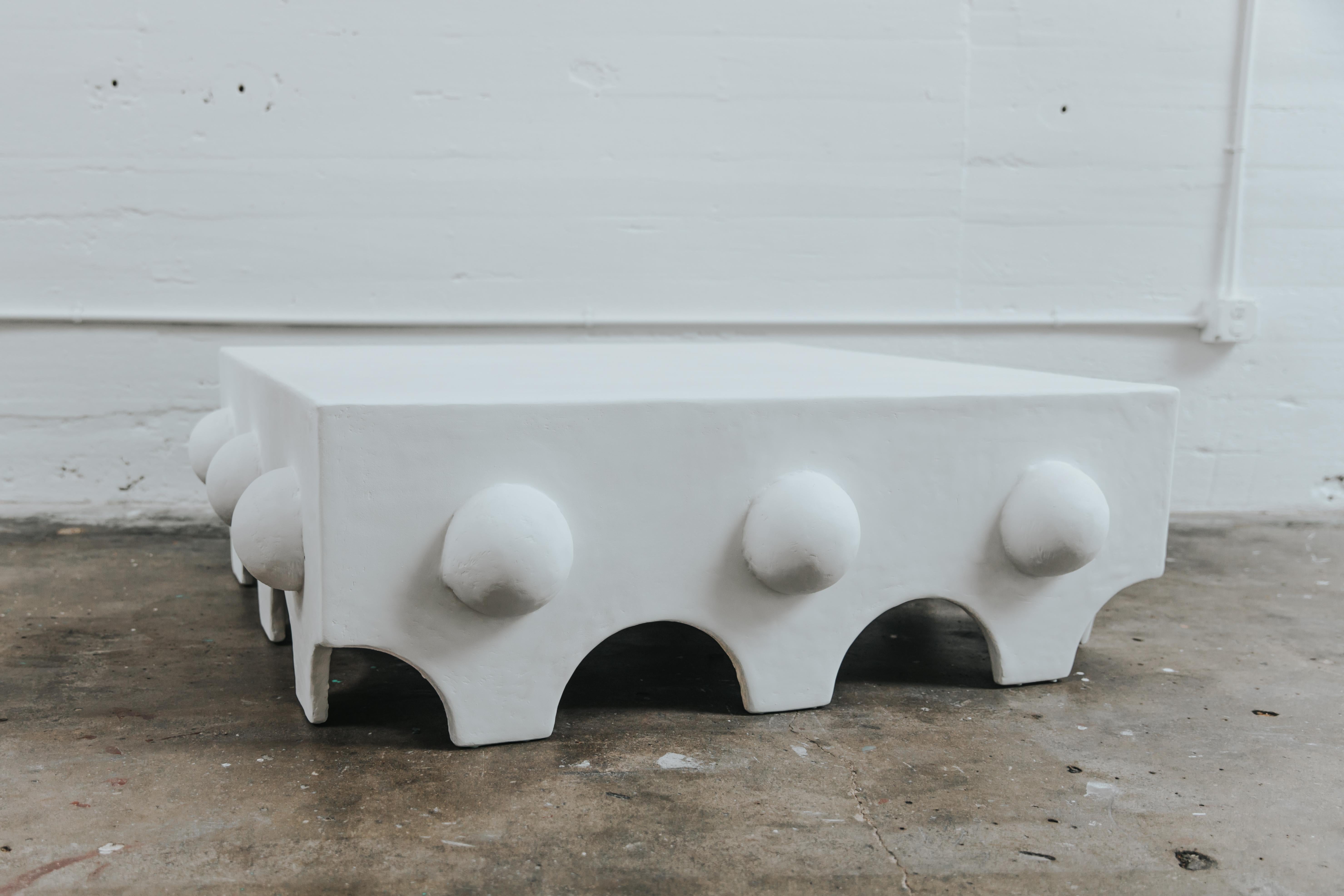 The Linda Coffee Table has a bold architectural presence that can anchor any living room. The oversized piece is covered in a complex plaster and paint mix and adorned with 12 sculptural cast plaster semi-spheres supported by a wooden base