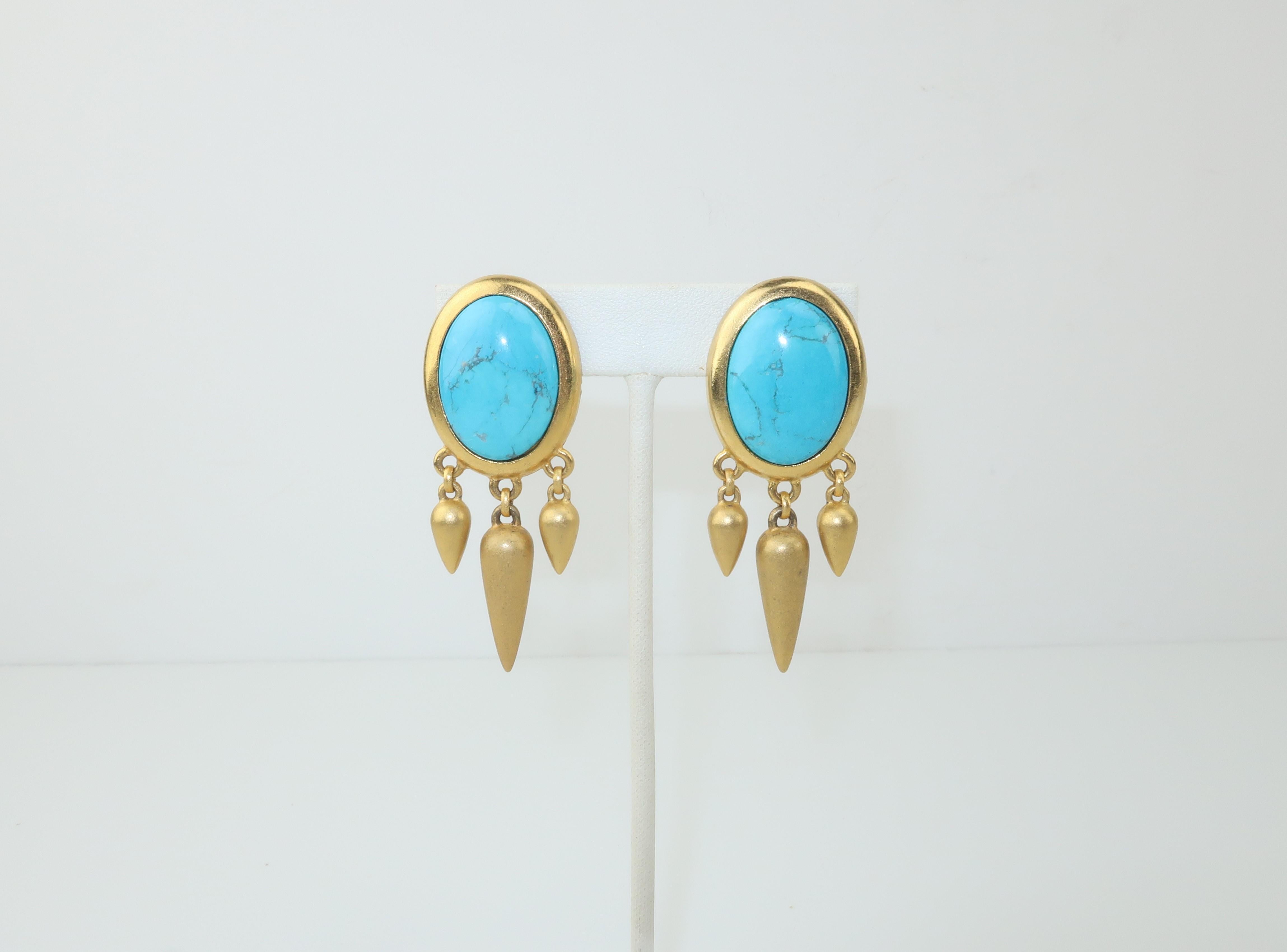 Linda Levinson combines modernity with a nod to a Victorian aesthetic with these C.1990 clip on earrings fabricated from a matte gold tone metal with an oval turquoise glass base accented by bullet shaped dangles.  Signed to the back and in very
