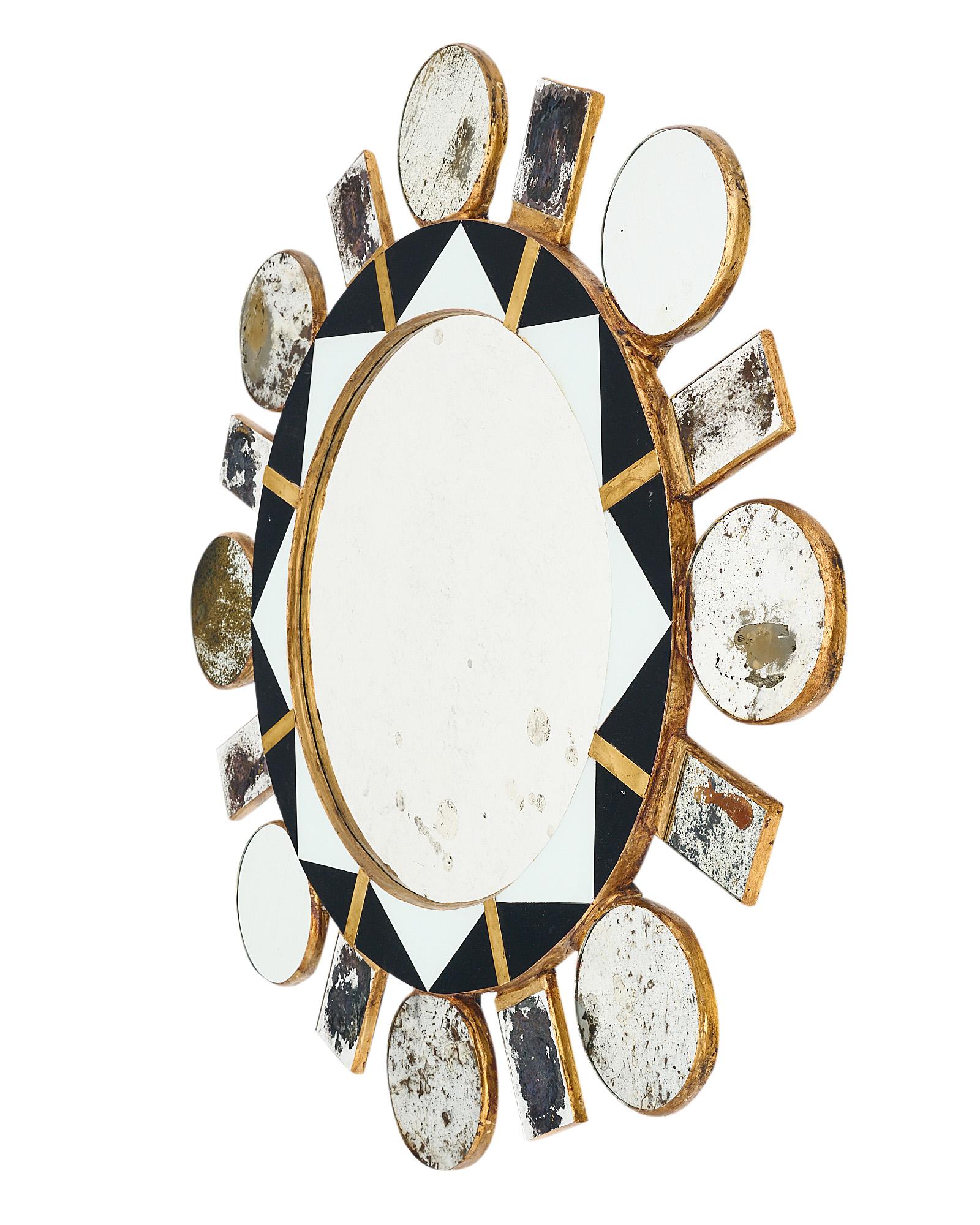Modernist sunburst in the style of designer Line Vautrin made with a wooden structure and antiqued mirror rays. There are circular and rectangular rays emanating from a central circular mirror. The central mirror is framed with black and white glass