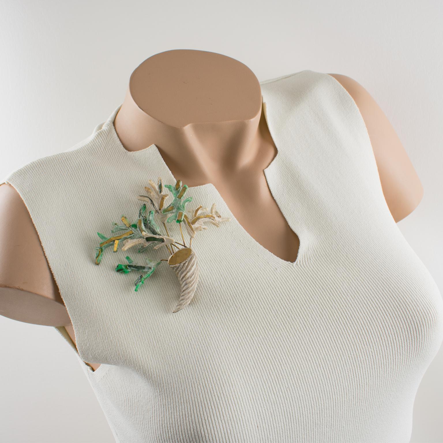 Este elegante alfiler broche de Line Vautrin Talosel presenta una cornucopia o cuerno de la abundancia con ramas de formas dimensionales en Talosel blanco y verde, incrustado de cristal espejado verde y dorado y metal dorado. 
Vidrio y Talosel, una