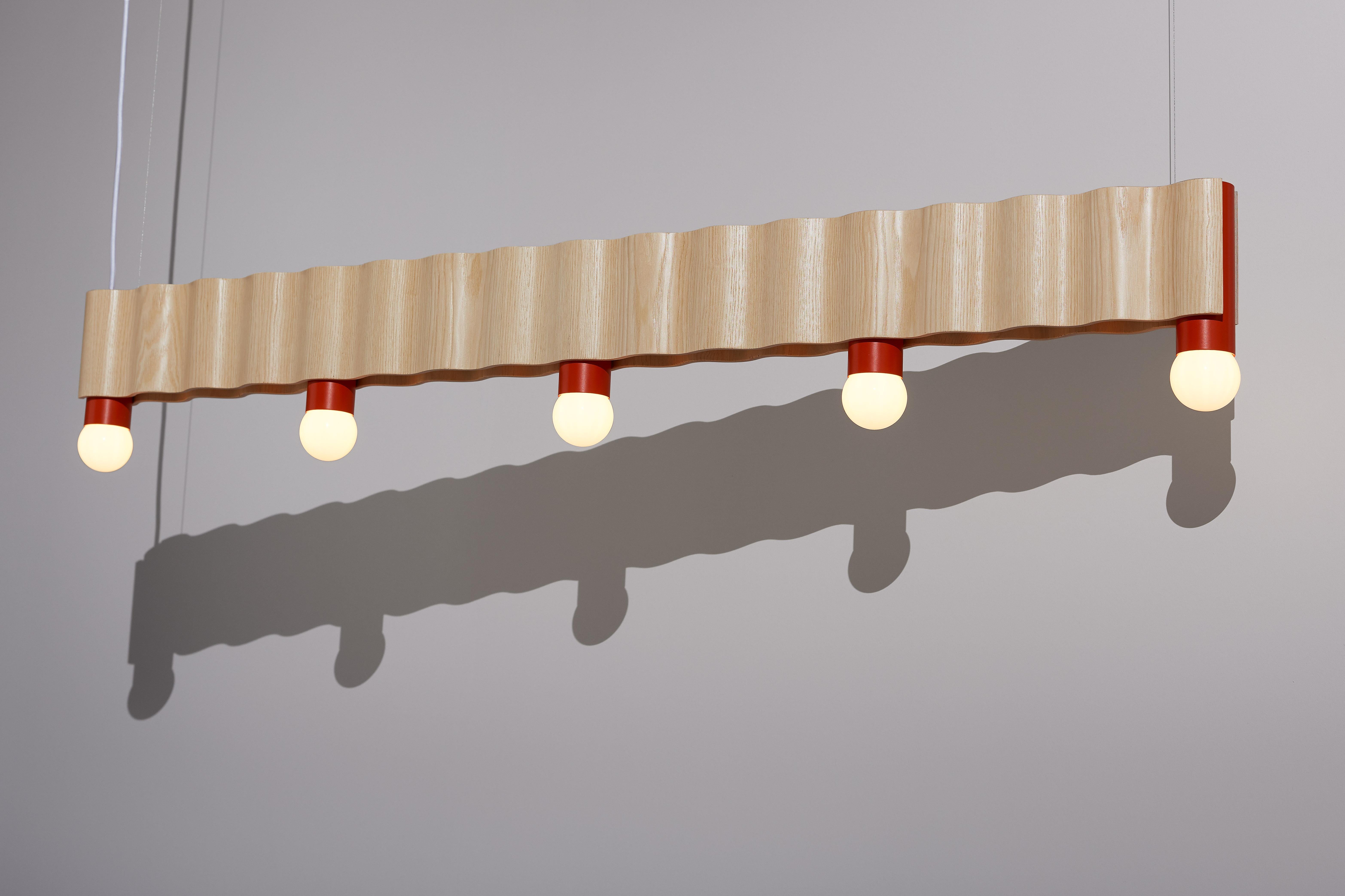 Linear corrugation pendant light (5 bulbs) made from natural ash veneered plywood (clear coated) and vermilion red powder-coated aluminium tubes.

Created in collaboration with Tino Seubert.

The linear pendant also comes as a shorter 4-bulb