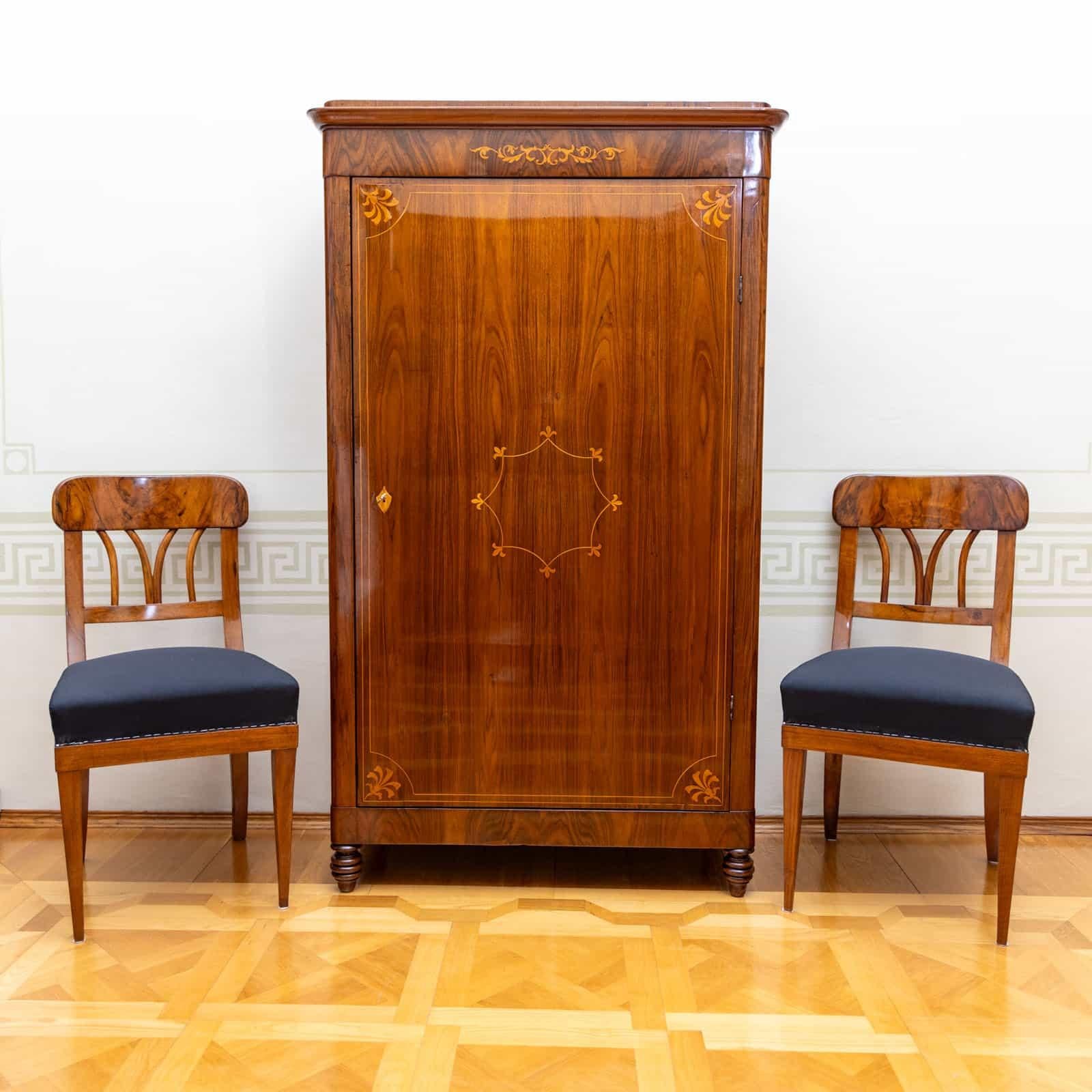 Single-door cabinet on turned legs with smooth doors and rounded corners. The cabinet is veneered in walnut and features elegant thread inlays and leaf decorations on the front. The cabinet has been restored and polished by hand. The interior