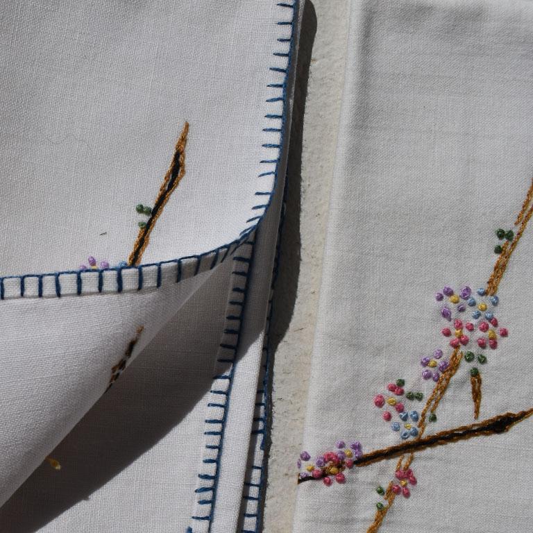 A set of 6 hand embroidered linen napkins with a stitched floral detail. Update your tableware with this pretty set of table napkins. Each piece is in white, with a blue stitched border around the edges. At each corner, is a branch of pink, blue and