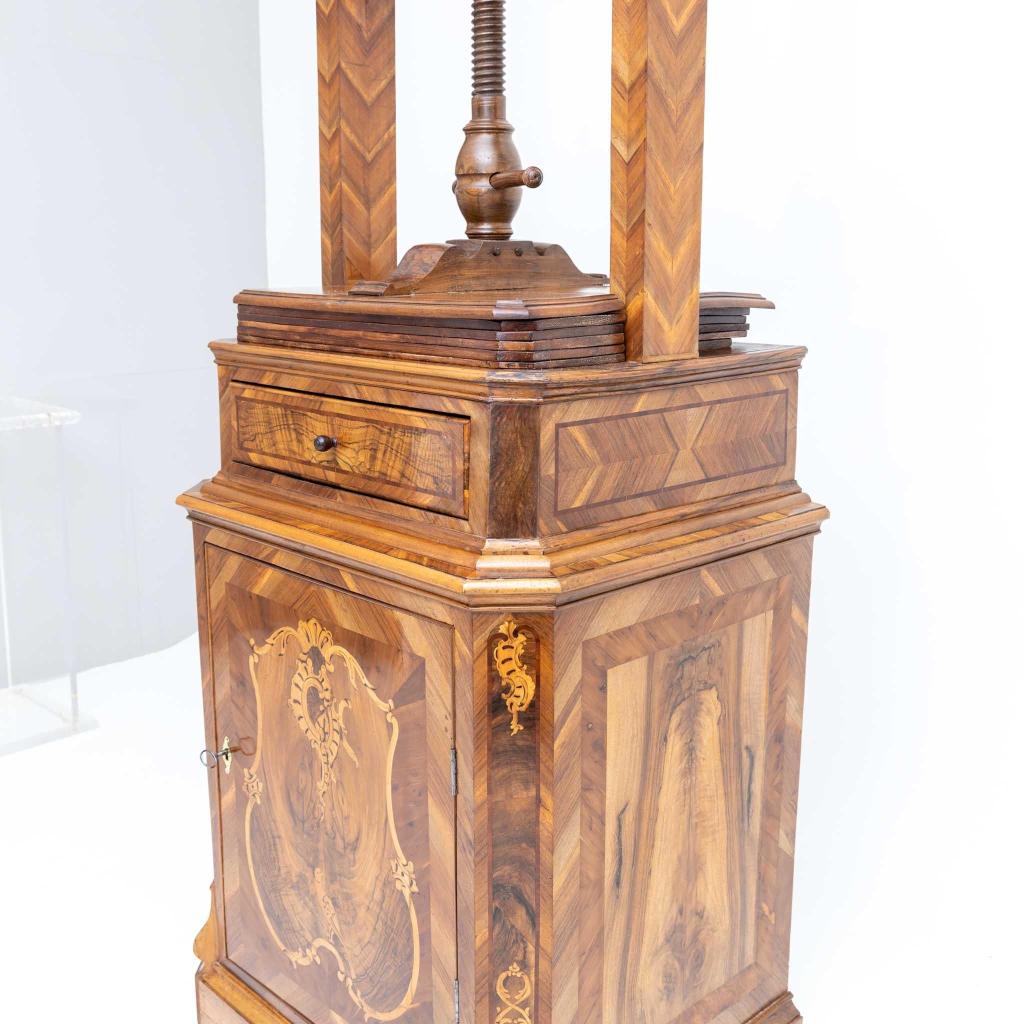 Laundry or linen press with six shelves for smoothing everyday linen such as tablecloths, bed linen, scarves and napkins. This spindle press features a single-door base and is equipped with a drawer. The exquisitely decorated body with walnut veneer