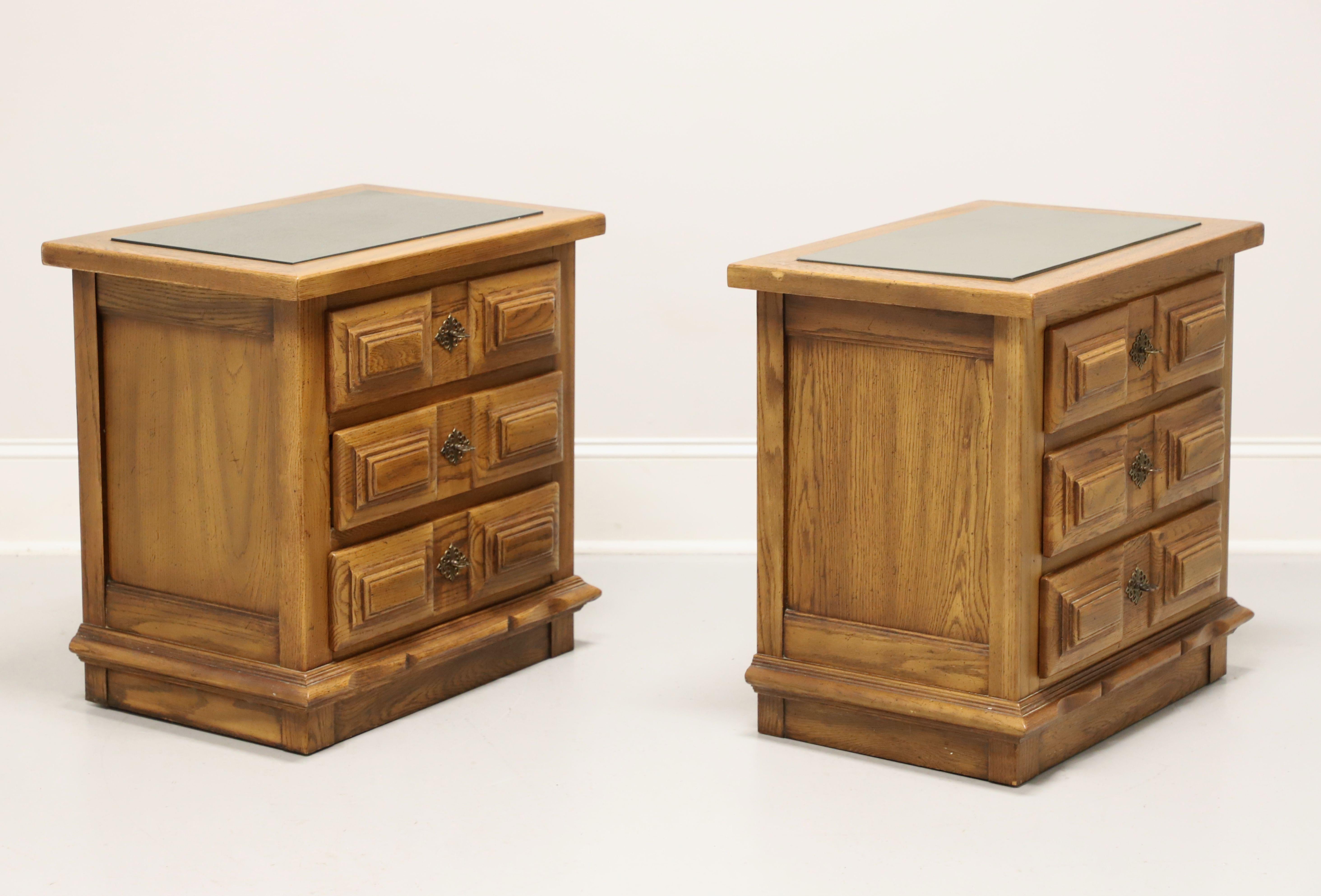 A pair of Spanish Colonial style nightstands by Link-Taylor, from their Espanol Collection. Solid oak with a lighter color slightly distressed finish, inset slate to the square edge top, brass hardware, raised & carved drawer fronts, and a
