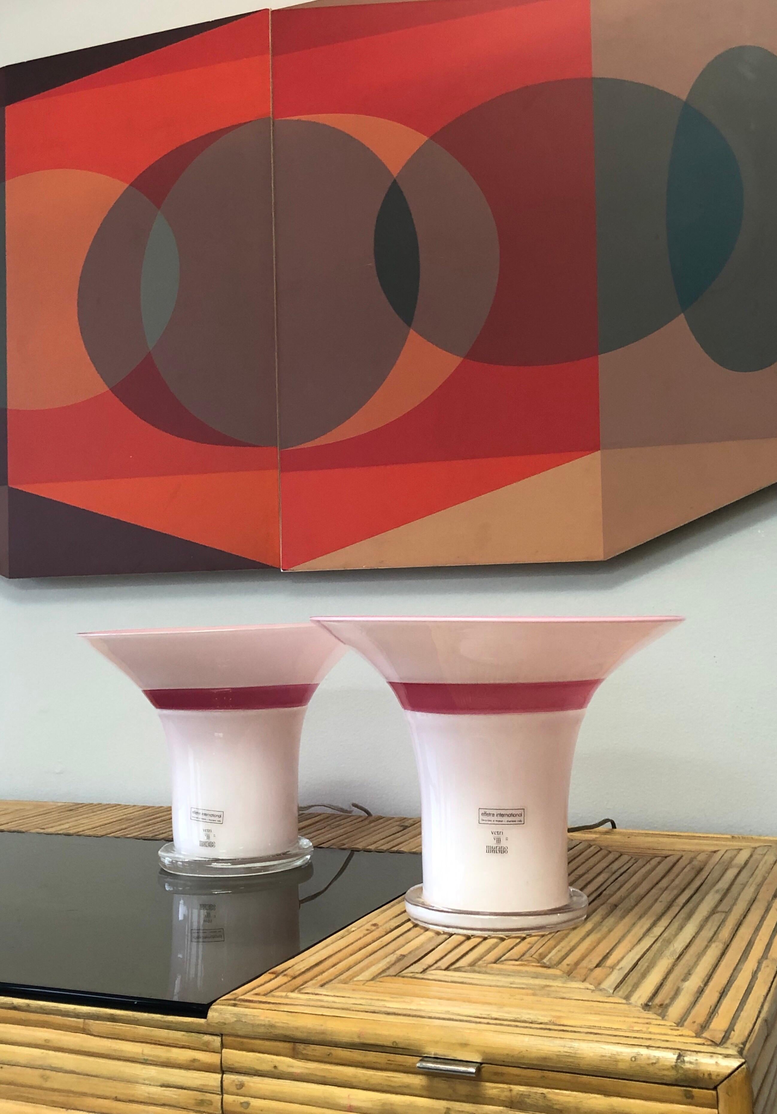 A pair of art glass lamps by Master art glass artist Lino Tagliapietra. White exterior with a light pink interior, raspberry band and clear base. Both are signed and dated 1982, also numbered 82 and 83 out of a limited edition of 100.