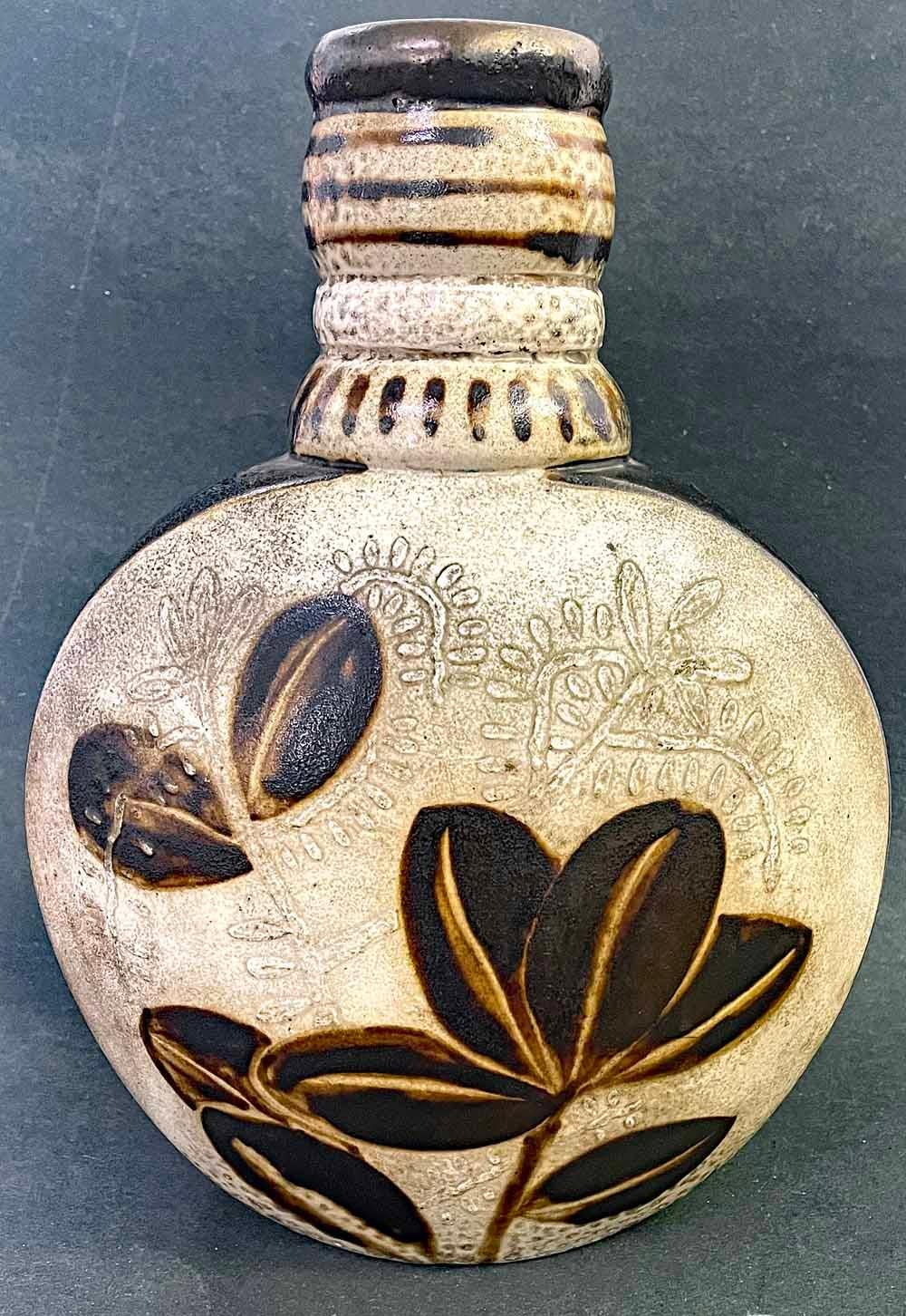 Large and substantial, this unique bottle-form vase features a lion and antelope on one side, and a branch with leaves on the other, all glazed in rich deep brown and ivory.  Each side includes botanical forms in low relief in the background.  The