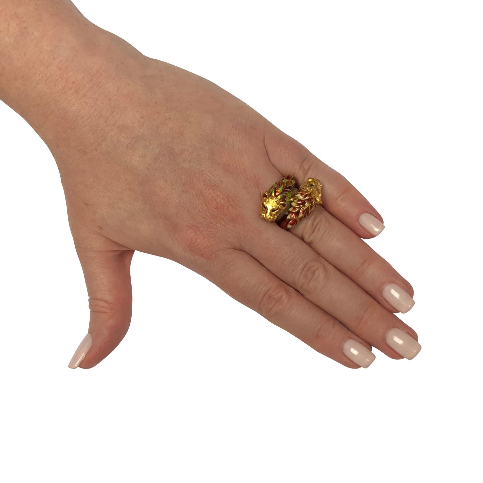 Intriguing lion head bypass ring crafted in 18 karat yellow gold featuring intricate and ornamental enamel ranging from electric crimson red to bright floral green and white. The ring measures 1 in width and at the widest and tapers to 3.96mm, the