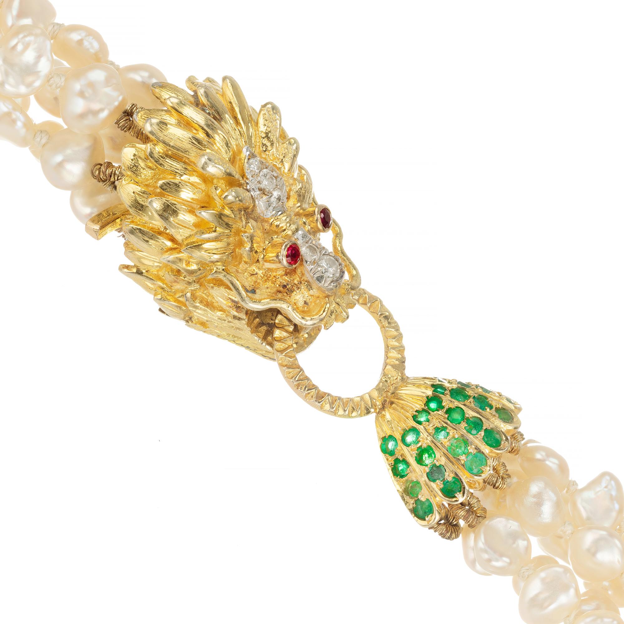 24 Inch 6 strand fresh water pearl necklace connected by a 14k yellow gold door knocker lion clasp with diamond nose and center of mane and ruby eye. The lion is grasping a round corrugated door knocker attached to an emerald accented pearl cup 

28