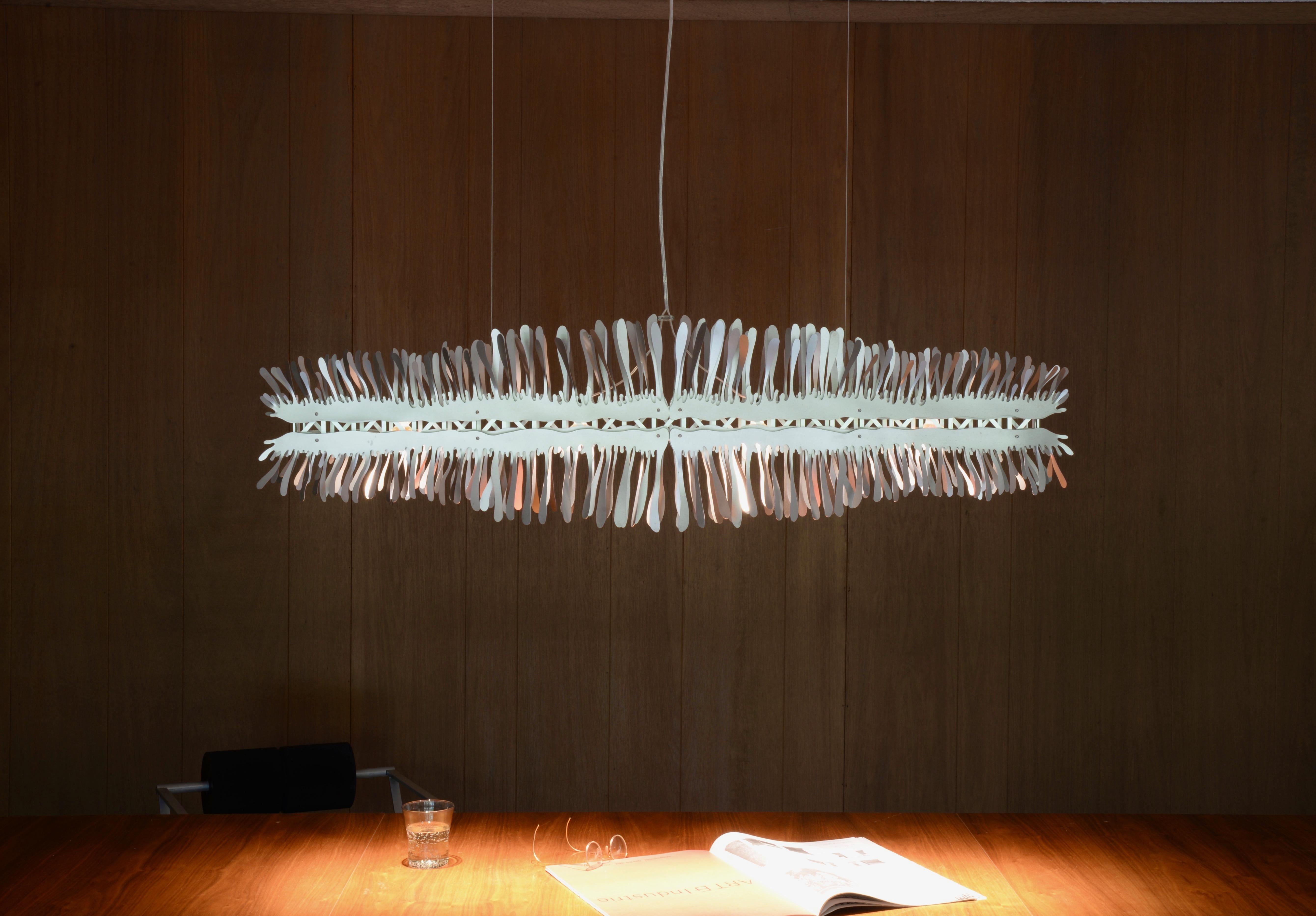 Liquid is a handmade stainless steel and aluminum linear chandelier providing warm direct LED illumination when suspended over a dining table, kitchen island or conference table. The sculptural exterior of Liquid is stainless steel with each element
