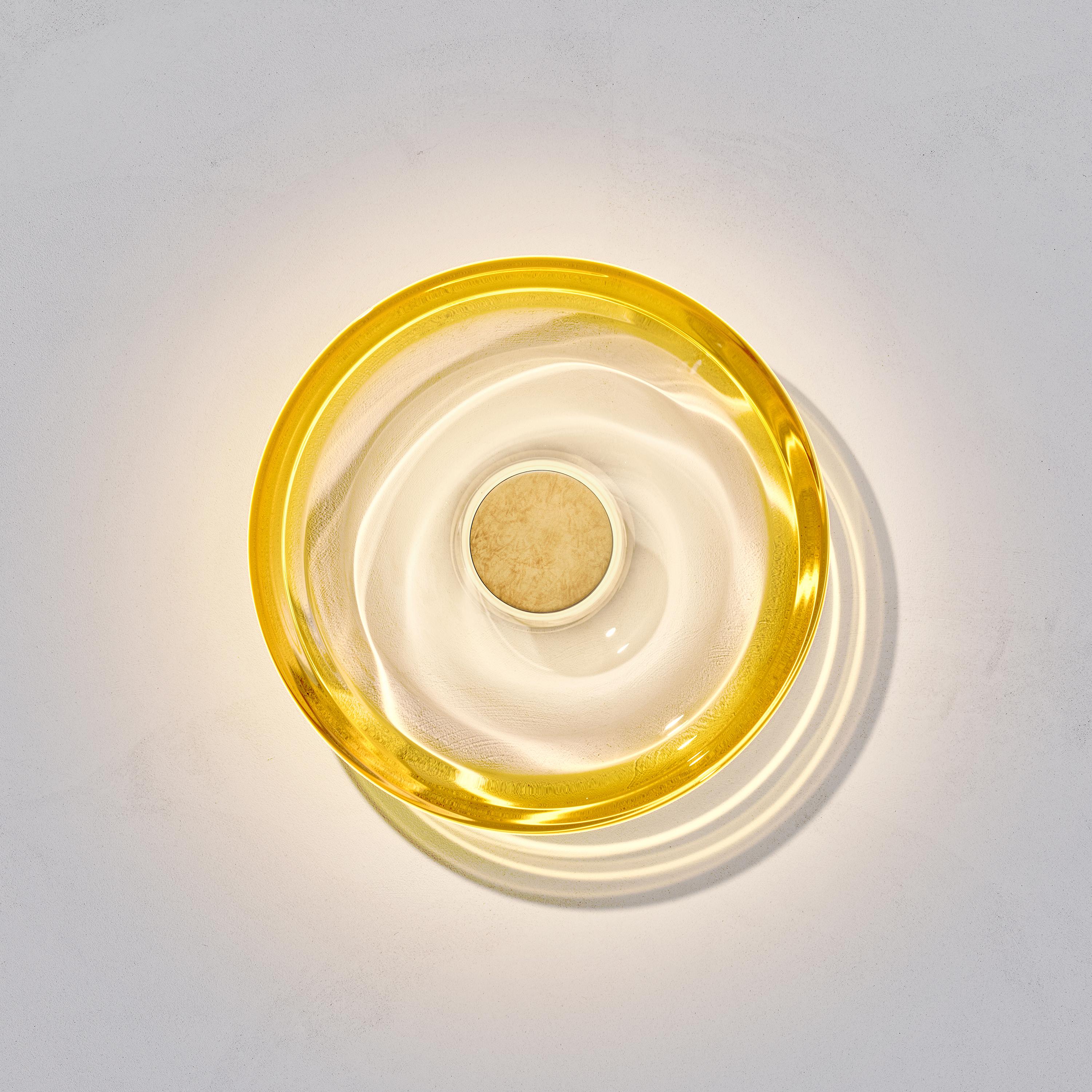 El aplique Liquid Amber ha sido diseñado por la artista internacional de la iluminación Eva Menz. Inspirado en las ondulaciones circulares y los reflejos que se crean en el agua, el cristal amarillo degradado se transforma en un bello candelabro