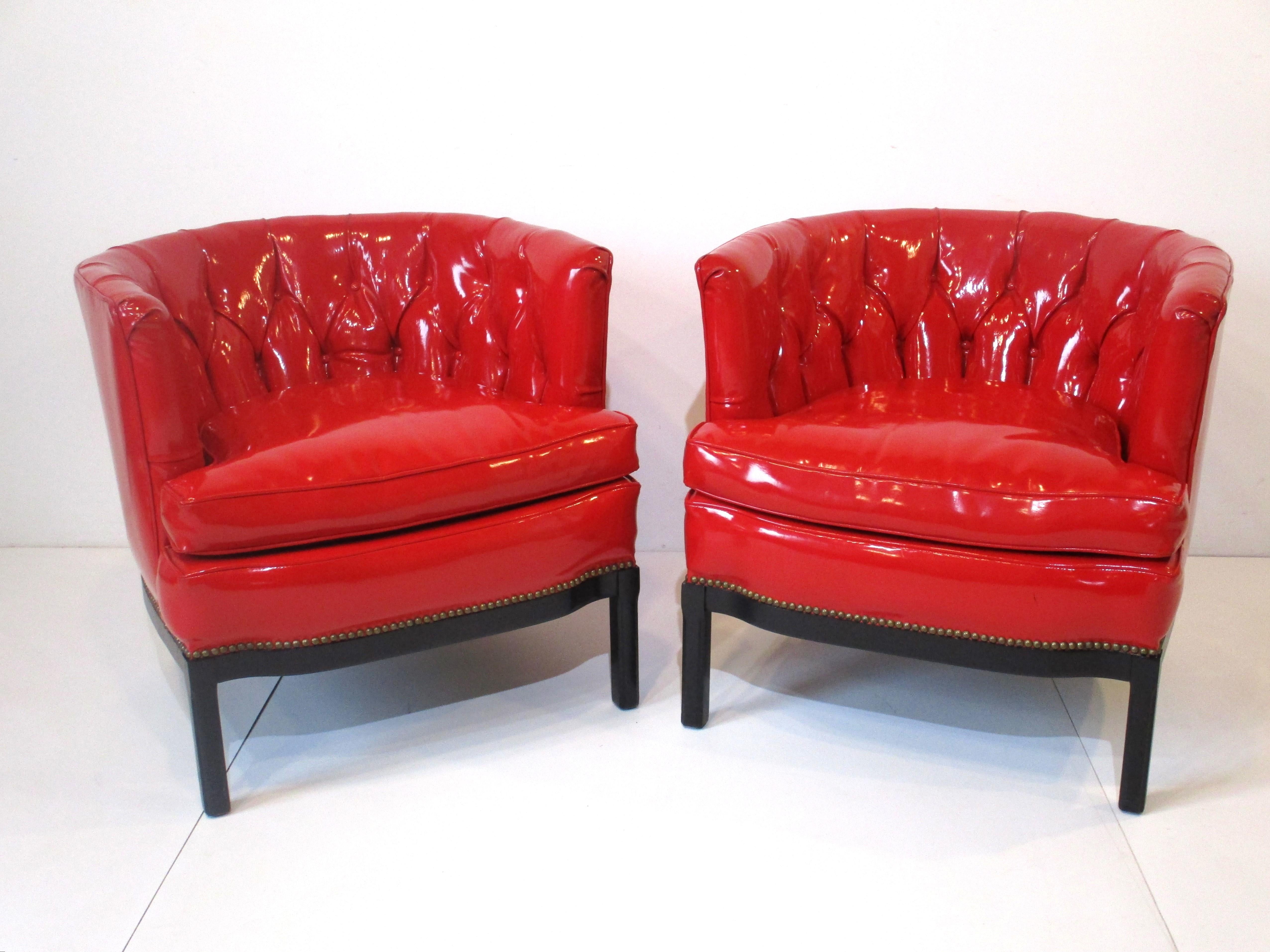 A fantistic pair of midcentury club chairs with tufted backs in liquid looking red Naugahyde having satin black legs and lower brass stud trim. Thess eye catching chairs with rounded backs are very comfortable and well crafted with perfect arm