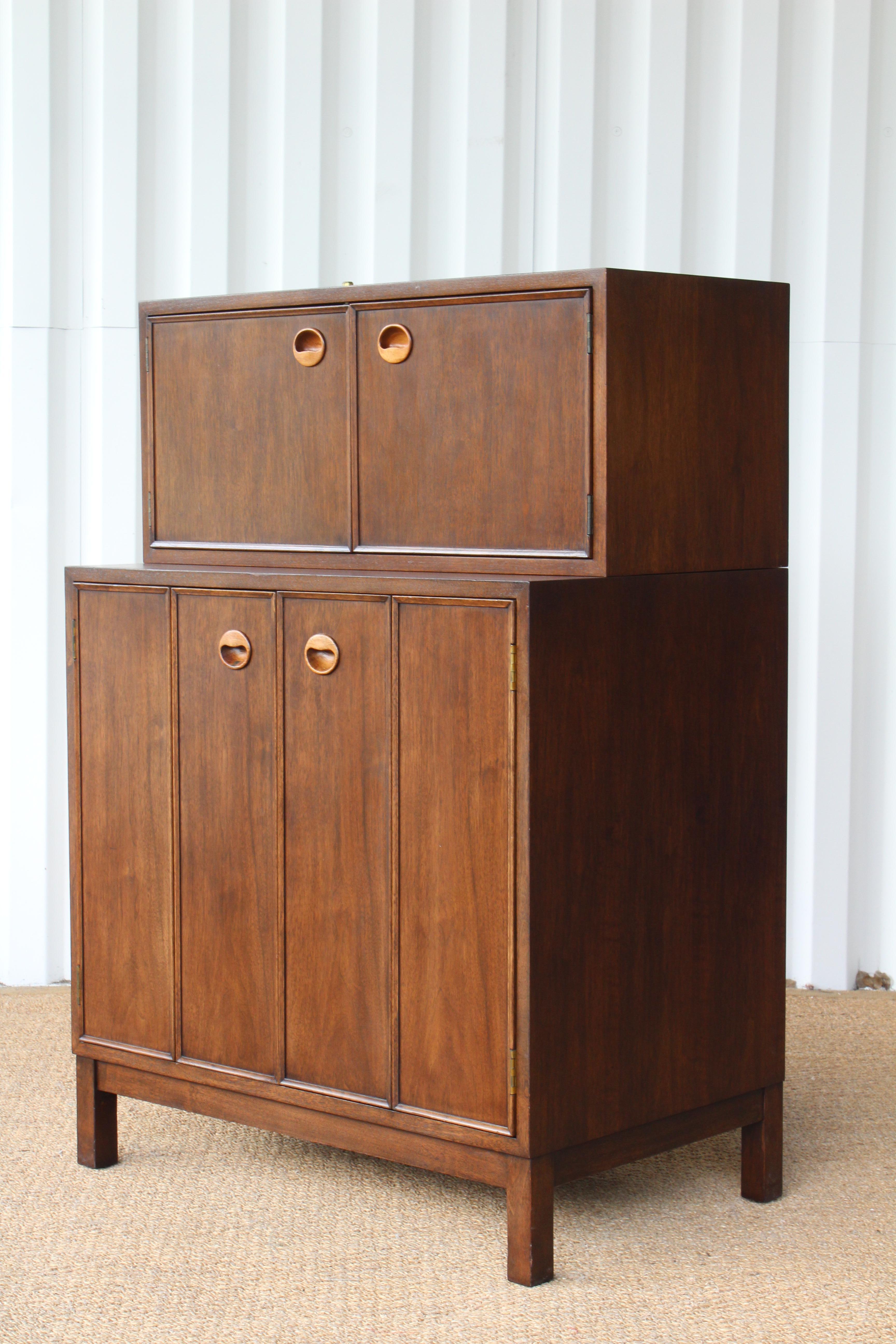Two-piece walnut liquor cabinet designed by Edward Wormley for Dunbar, USA, 1950s. Features accordion folding doors, rosewood handles, and an interior adjustable shelf. Original keys include. Top cabinet locks. Can be used with or without top piece.