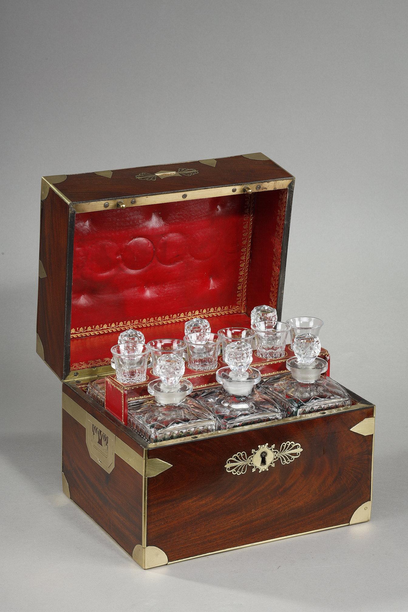 Flamed mahogany liqueur cellar with brass inlaid frame simulating box hardware. The side handles are also inlaid around a motif of two swans facing each other. The keyhole and opening handle are adorned with two palmettes. A monogrammed CG