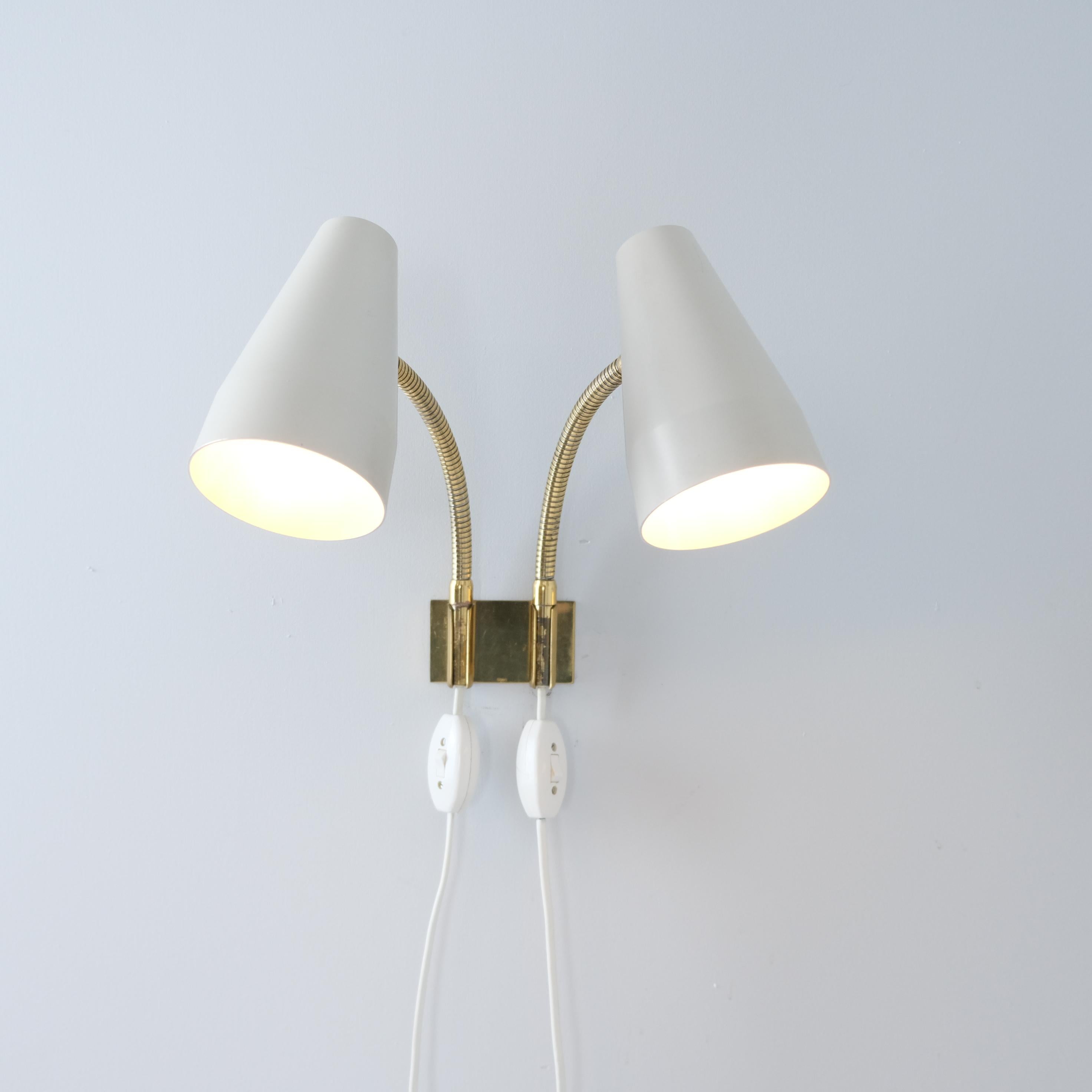 Un encantador aplique doble de Lisa Johansson-Papé para Orno, modelo 50-056-2, que combina detalles de latón con pantallas de metal pintado en su inconfundible estilo estético escandinavo, limpio y funcional. Las dos pantallas cónicas están montadas