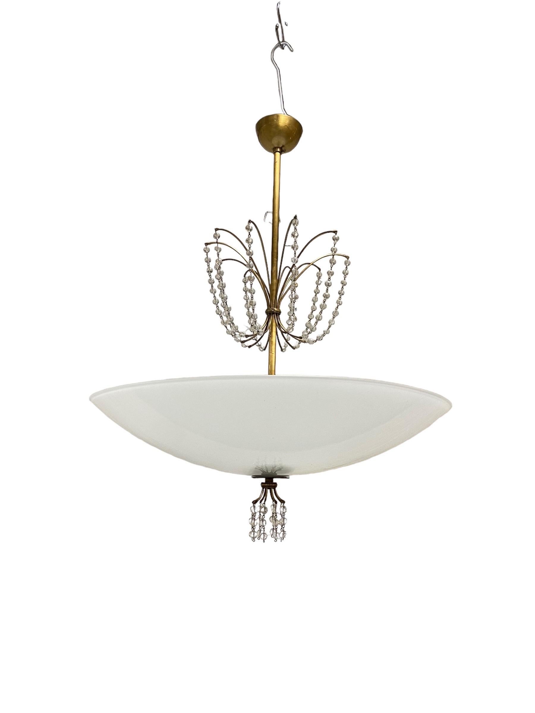 A beautiful Scandinavian Modern ceiling lamp model 1068 in brass, crystal and glass designed by Lisa Johansson-Papé and manufactured by Orno Oy in Finland in the 1940s-1950s. The lamp features crystals that hang like rain drops and are beautifully