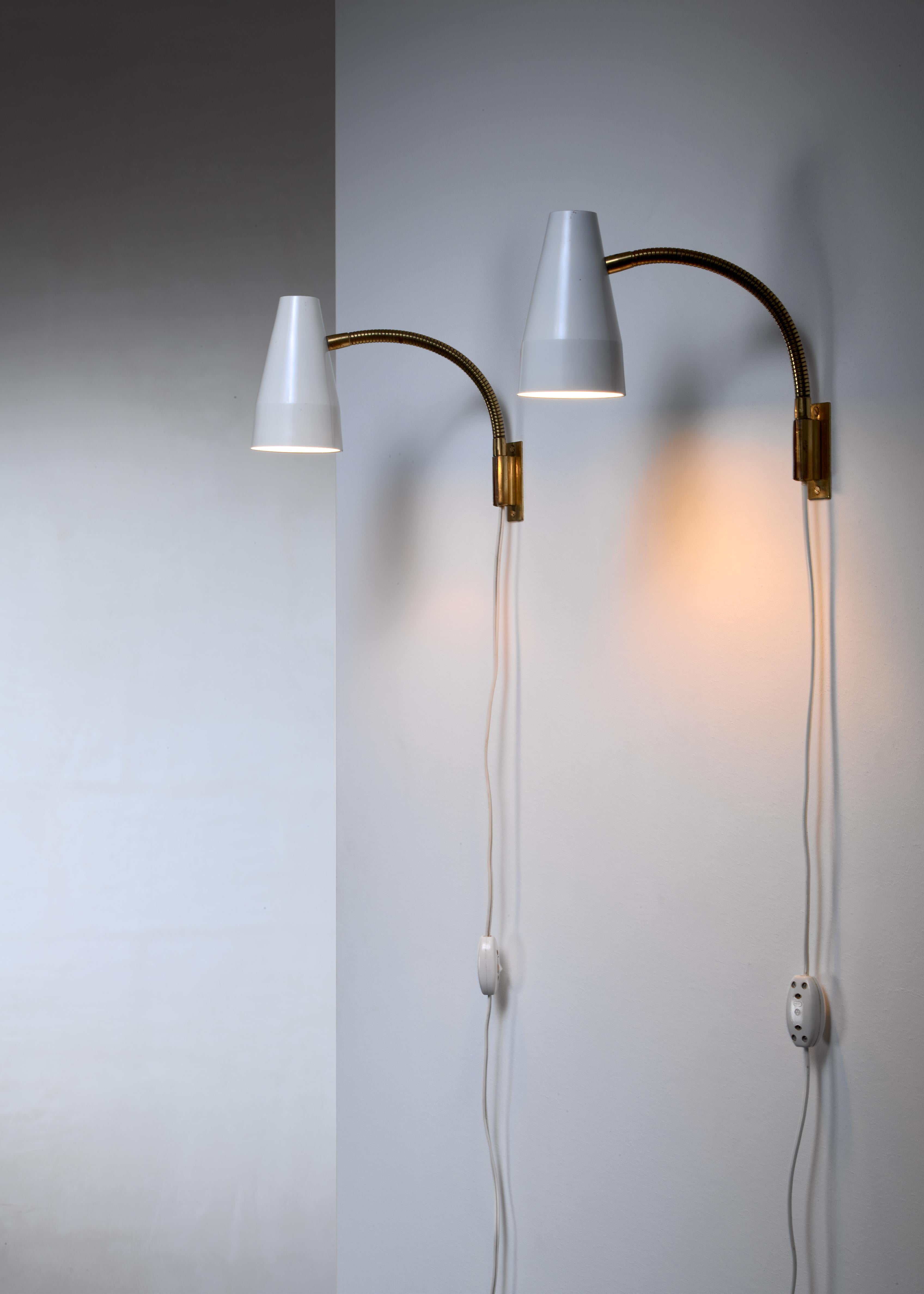 A pair of 1950s wall lamps by Lisa Johansson-Pape for Orno. The lamps have a flexible brass stem and a white lacquered metal hood. Marked by Orno and in a good condition.