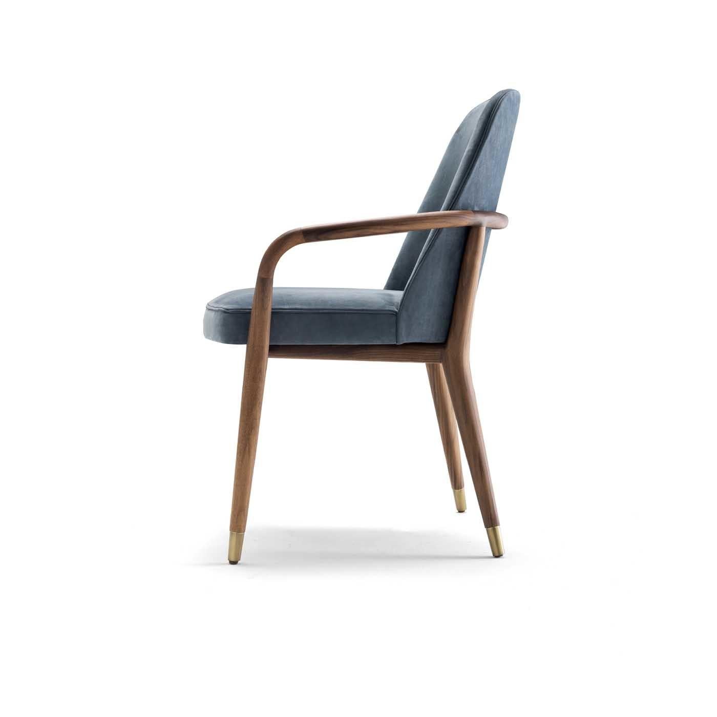 This elegant chair with armrests will add charm and elegance to a modern dining room or study. Its midcentury inspired design features a frame in solid American walnut boasting slanted back legs, and open armrests and metal feet with a satin brass